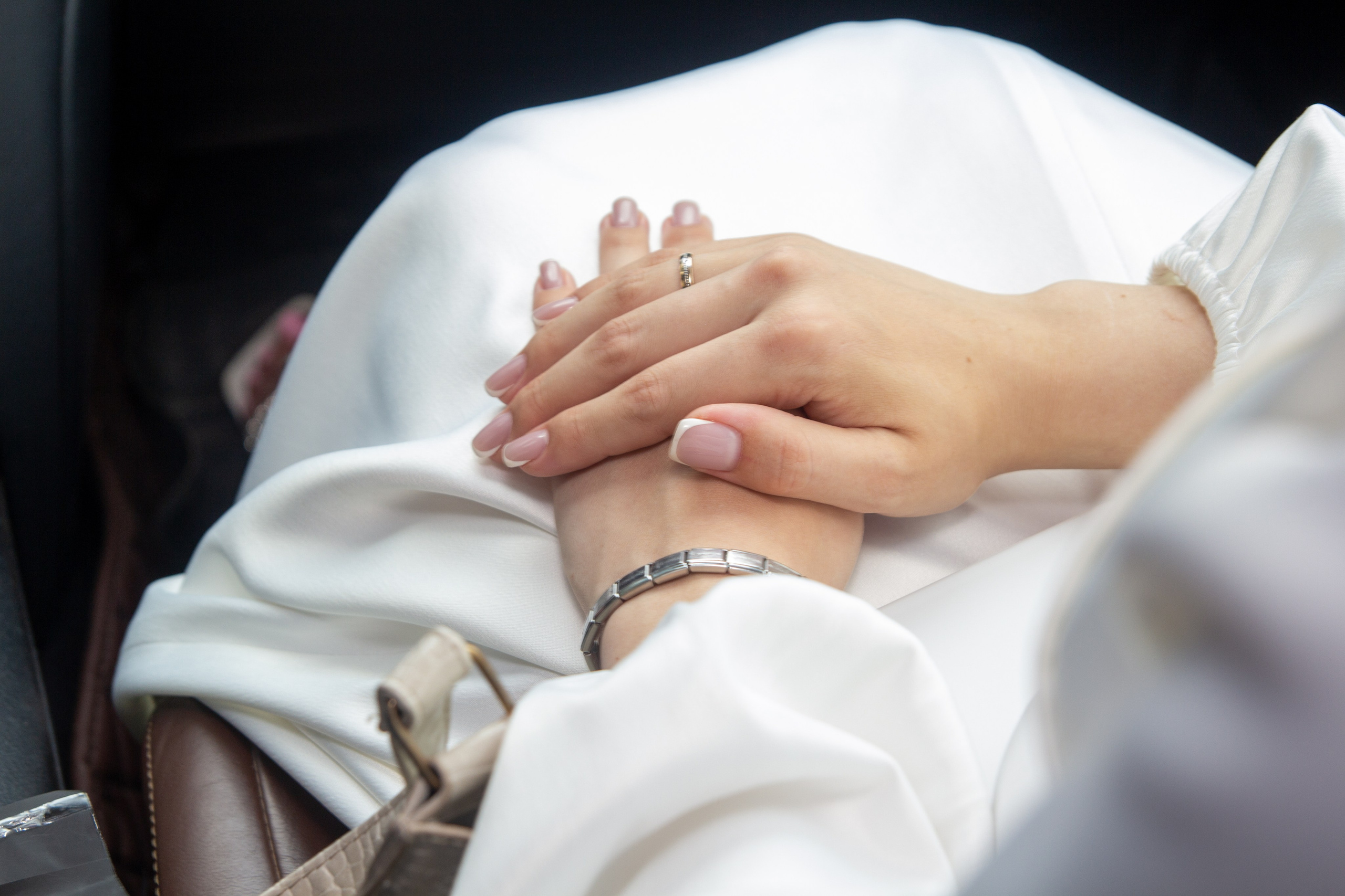 Сложенные руки жениха и невесты на коленях в машине — момент тишины и близости.