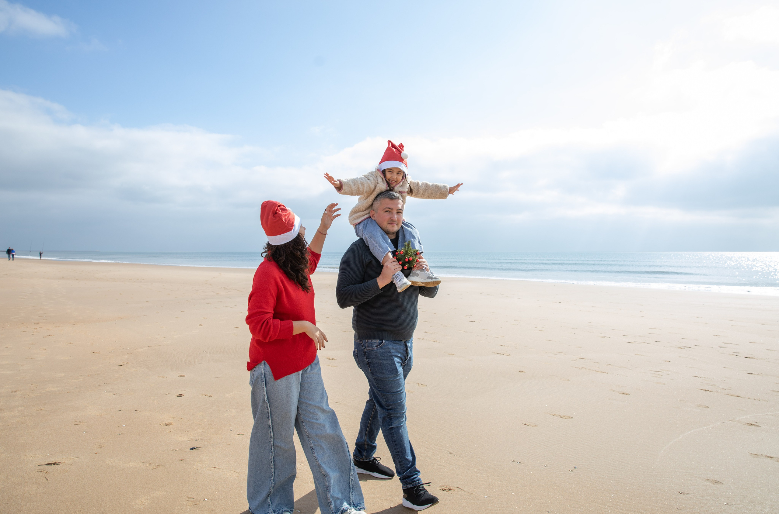 A happy family of three walking hand in hand along the sandy beach. Dad carrying his daughter on his shoulders, both laughing under the sun