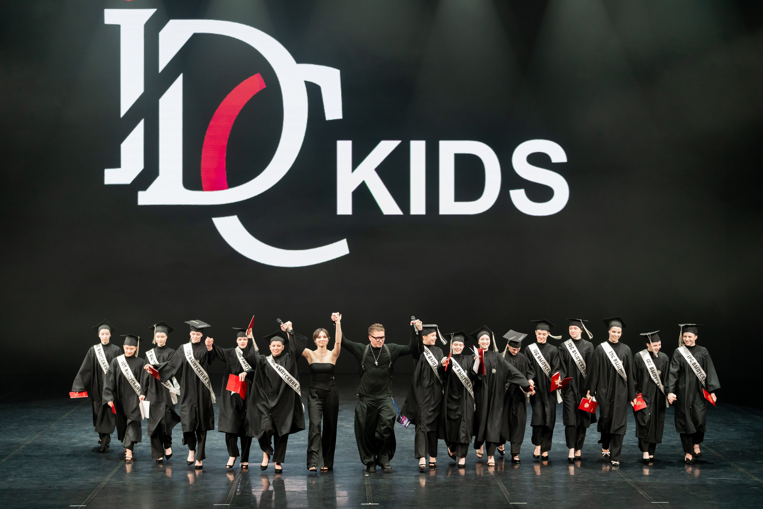 IDC Russia Kids выпускной – выпускники держатся за руки на фоне логотипа IDC, автор Мальцев Евгений, Санкт-Петербург.