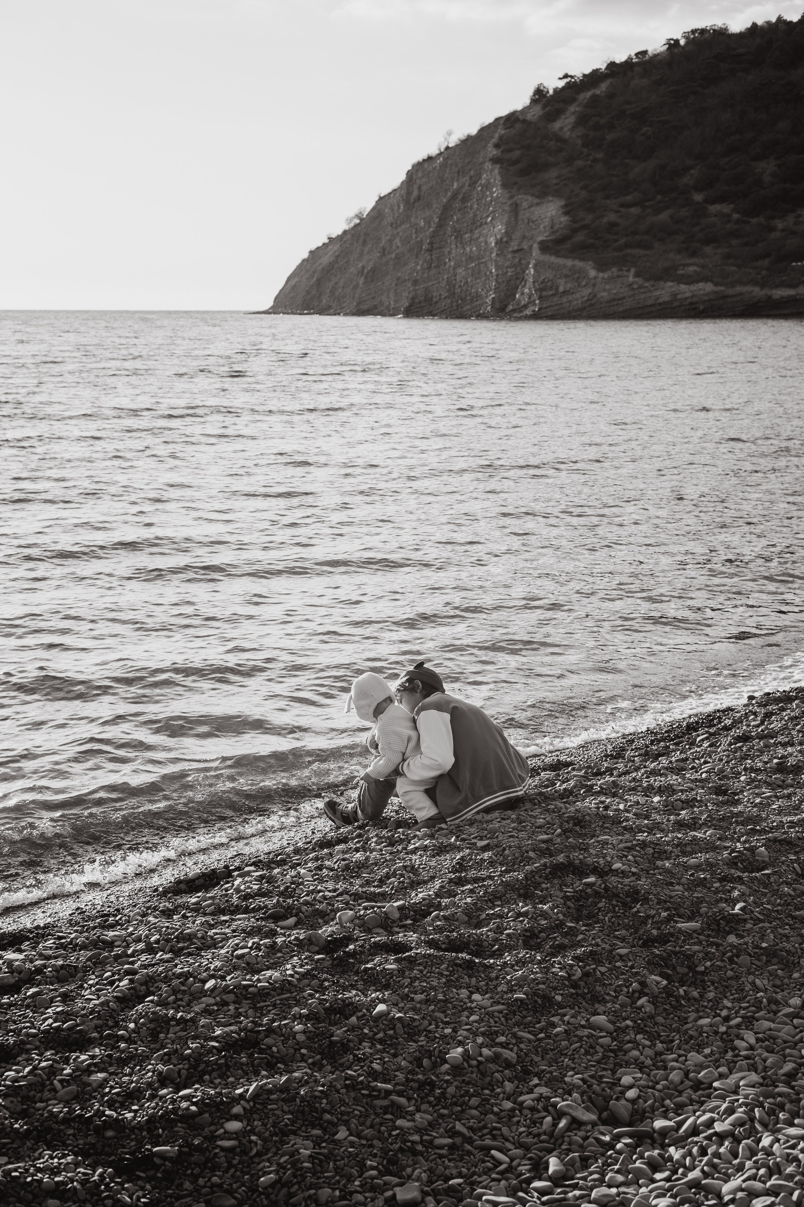 Брат с маленькой сестрой сидят на берегу моря и любуются им