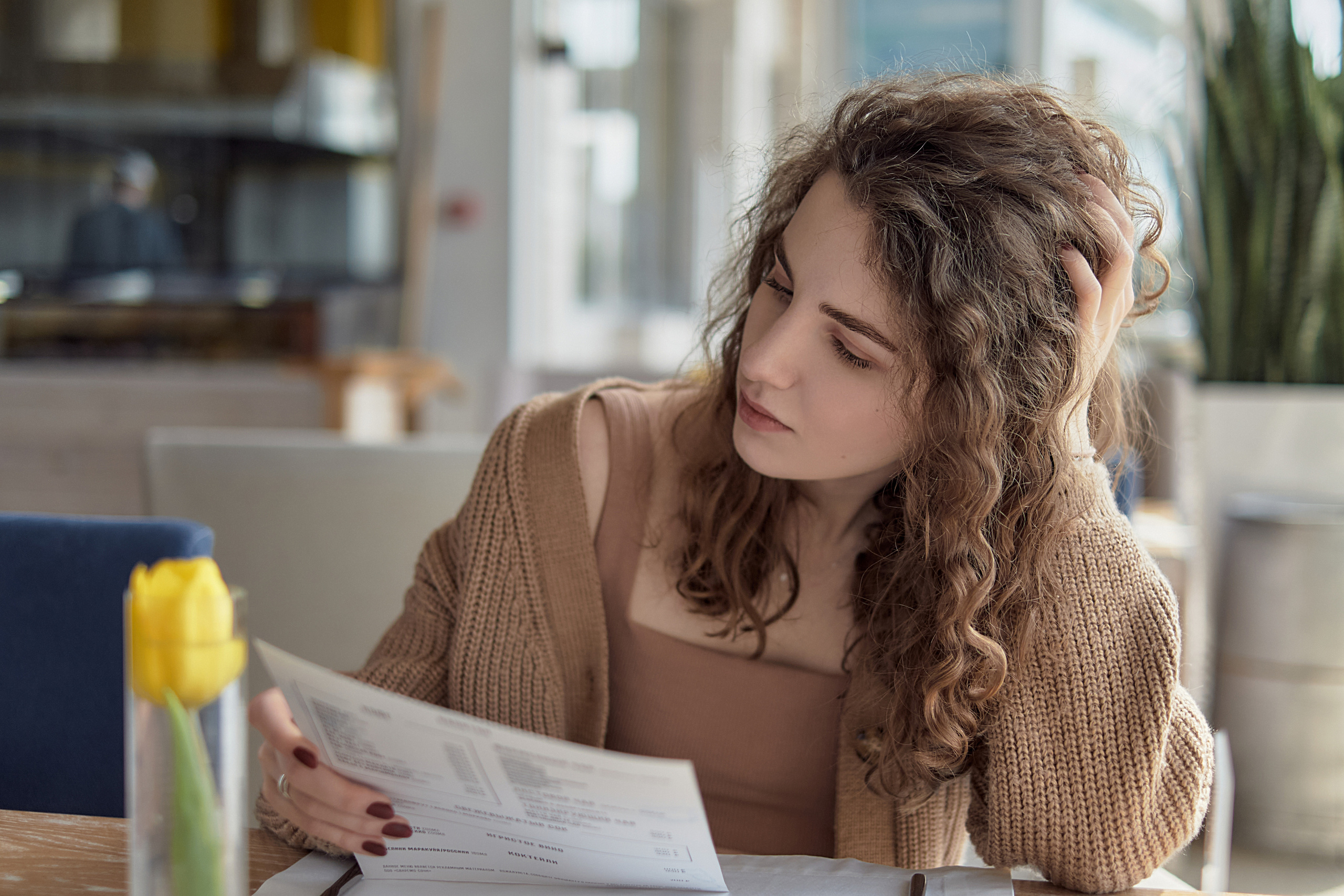 Девушка с кудрявыми волосами сидит в ресторане и читает меню