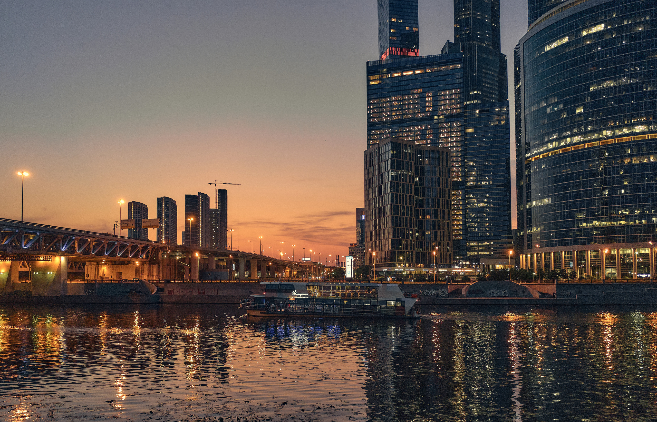 Мост и высотки Москва-Сити со светящимися окнами офисоф на фоне вечернего неба с отражением в Москве реке