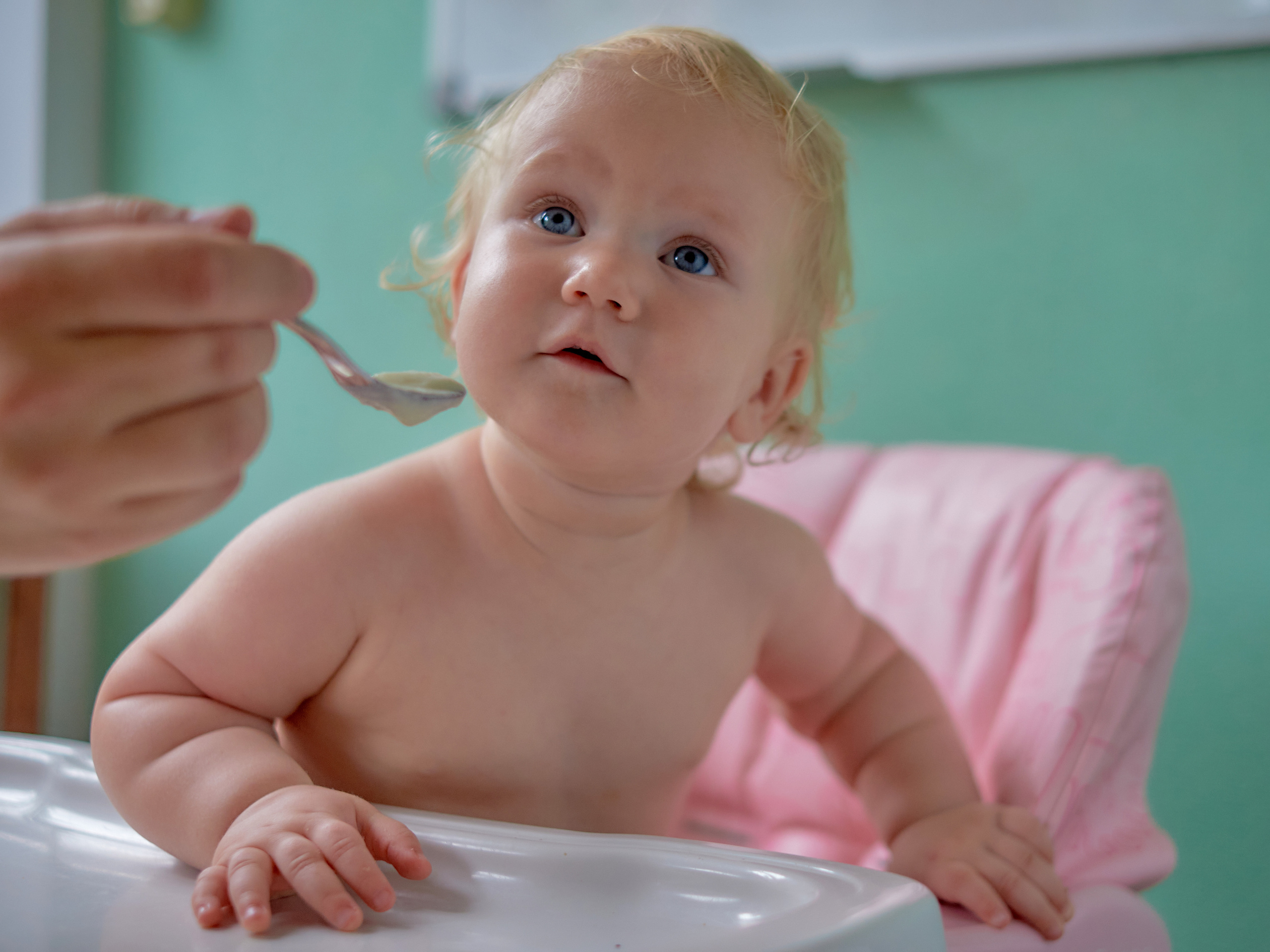 Улыбающегося младенца с голубыми глазами кормят с ложки детским питанием