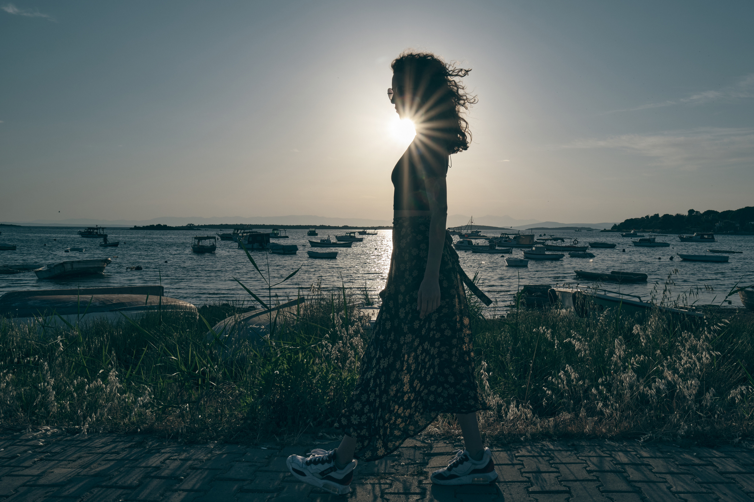 Девушка с развивающимися волосами на фоне заходящего в море солнца идет вдоль берега 