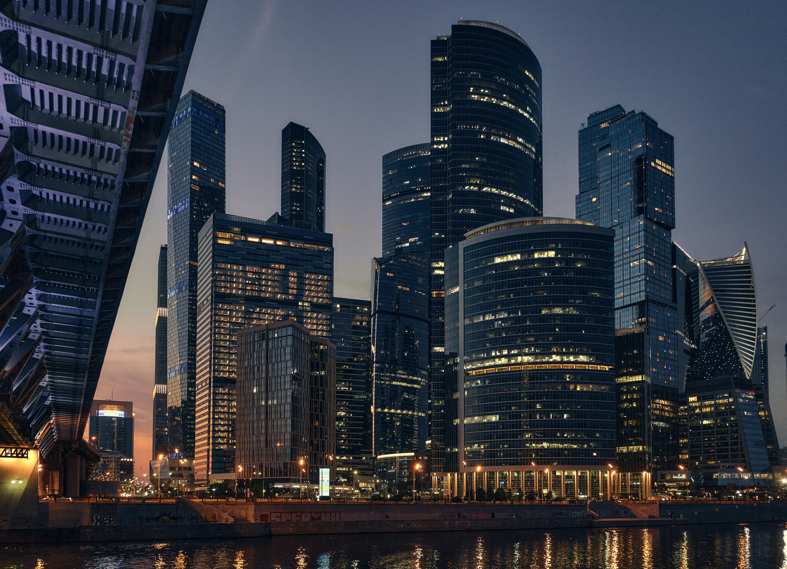 Архитектура Москва-Сити со светящимися окнами офисоф на фоне вечернего неба с отражением в Москве реке