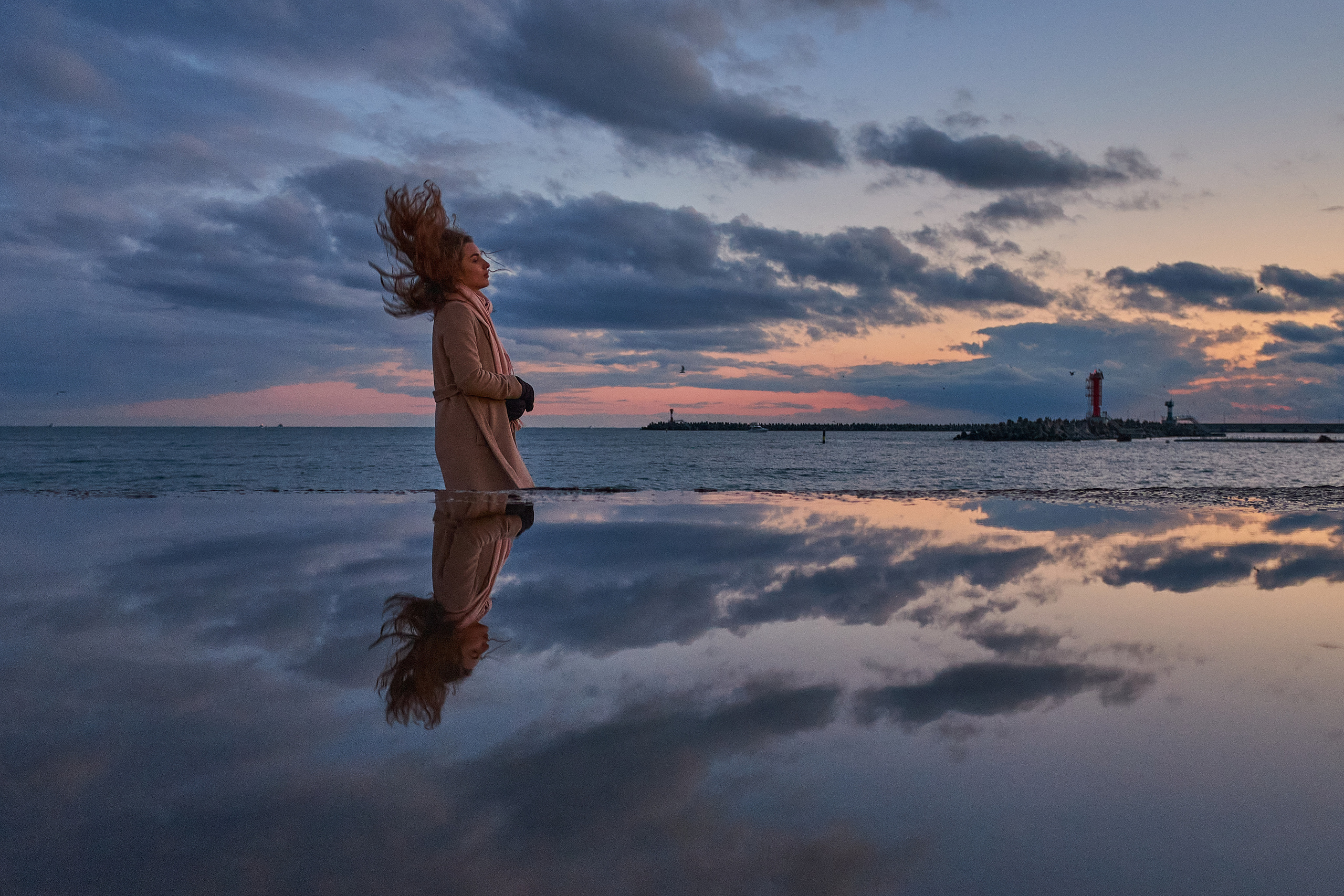 Девушка с развивающимися на ветру волосами на фоне заката отражается в водной глади