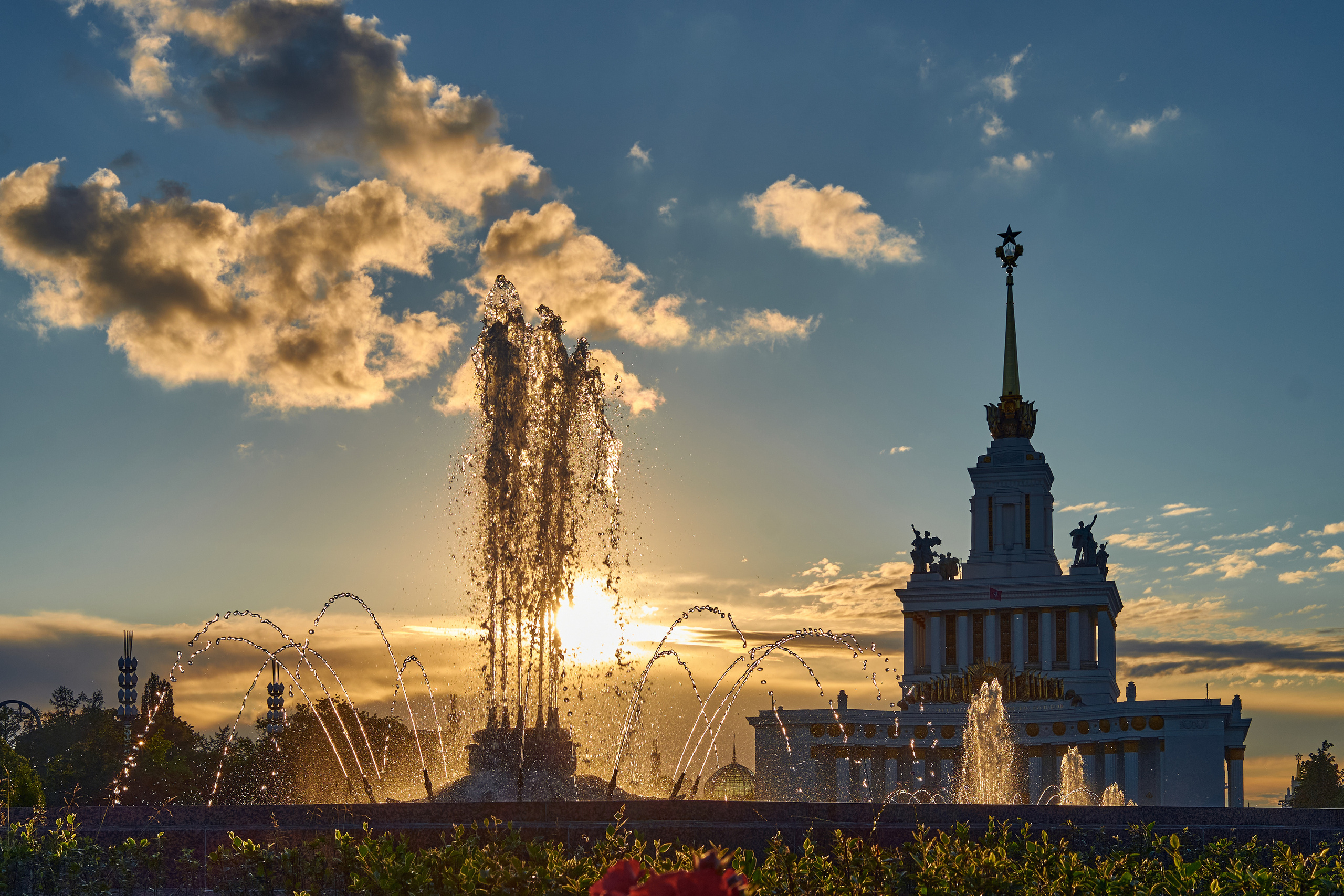 Фонтан в парке ВДНХ на фоне заката и здания центрального павильона 