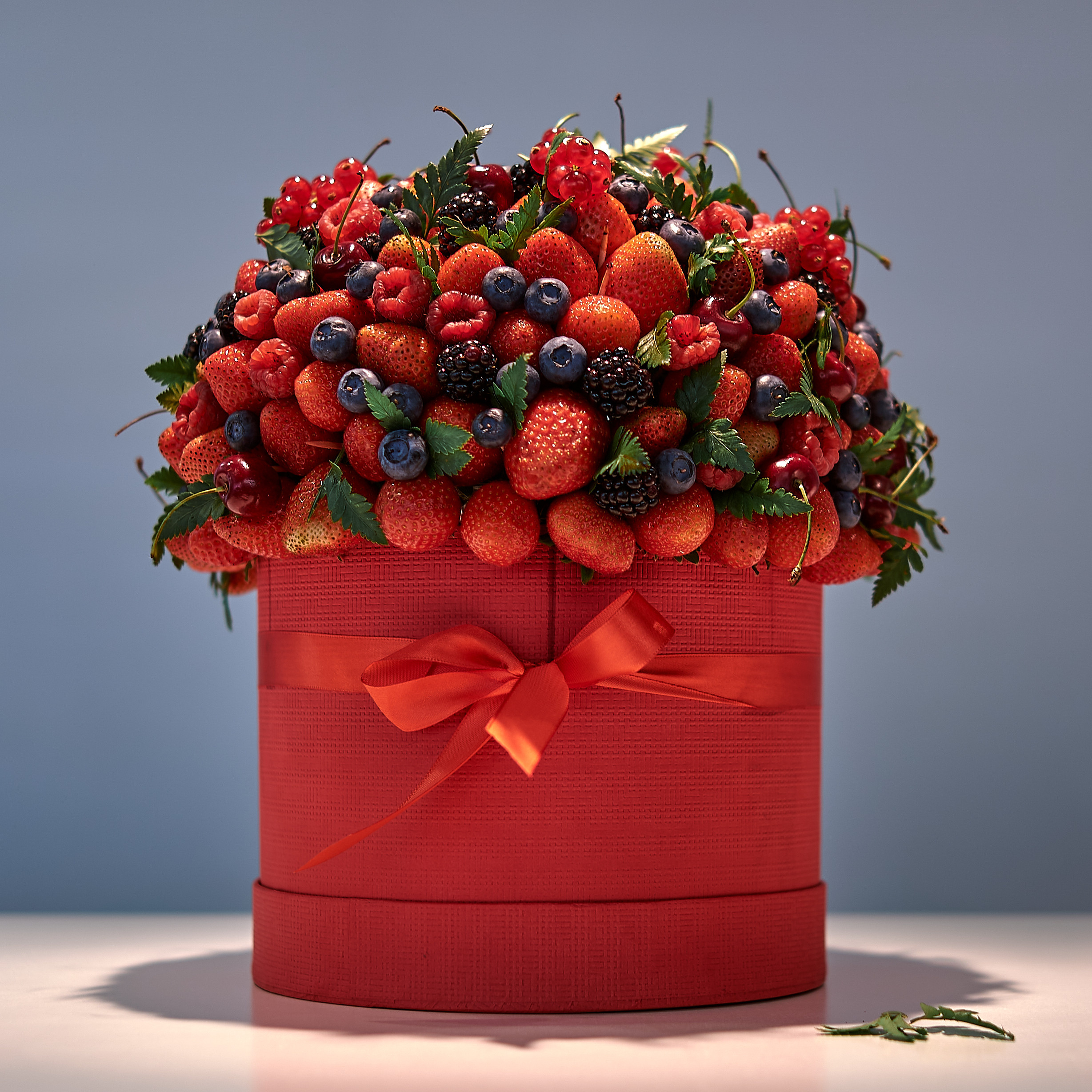 Букет из свежих ягод красиво оформлен в красную круглую коробку с красной лентой завязанной бантиком