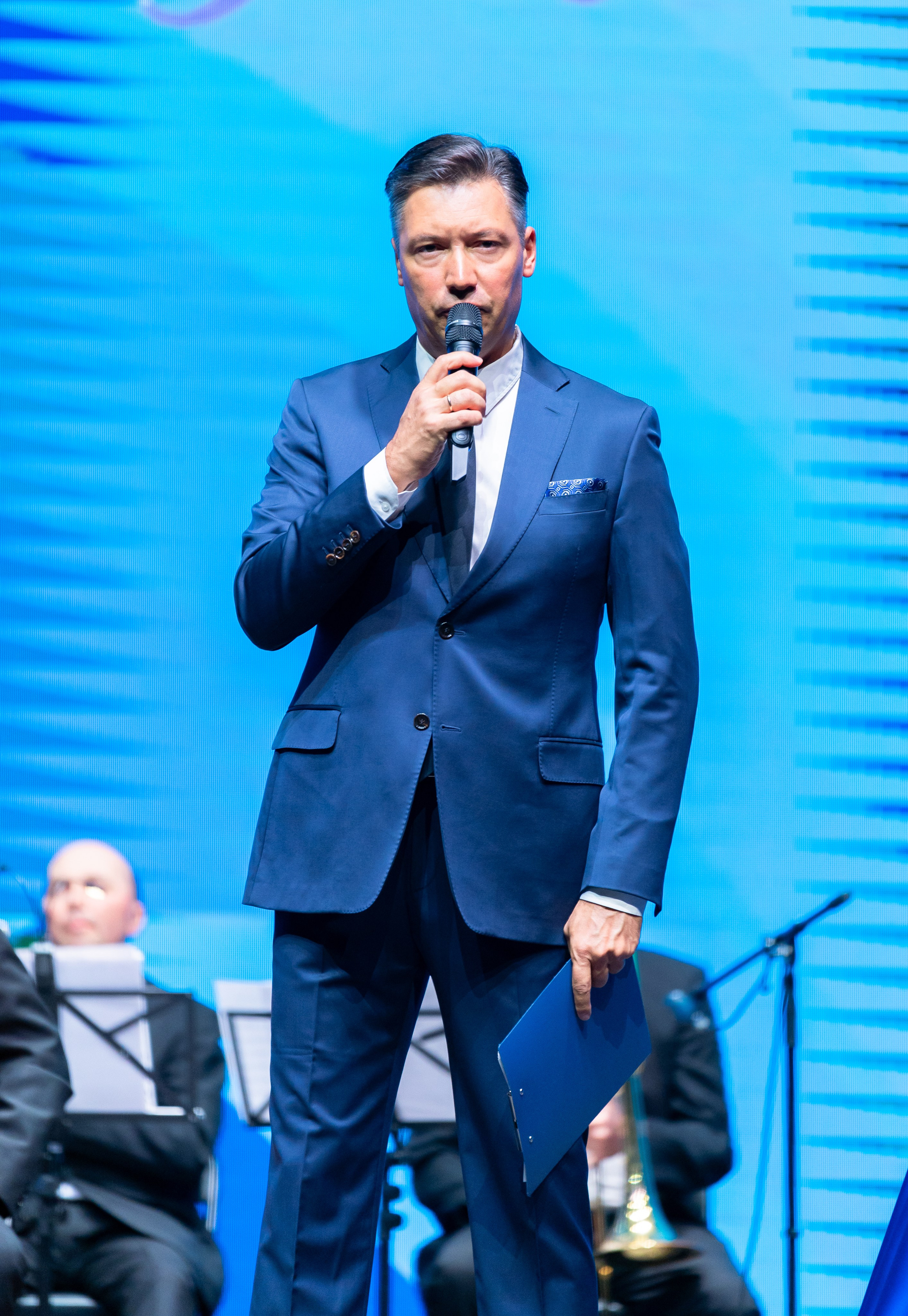 Мужчина в синем костюме с микрофоном ведёт концерт. День местного самоуправления в Санкт-Петербурге. Фото Евгения Мальцева.