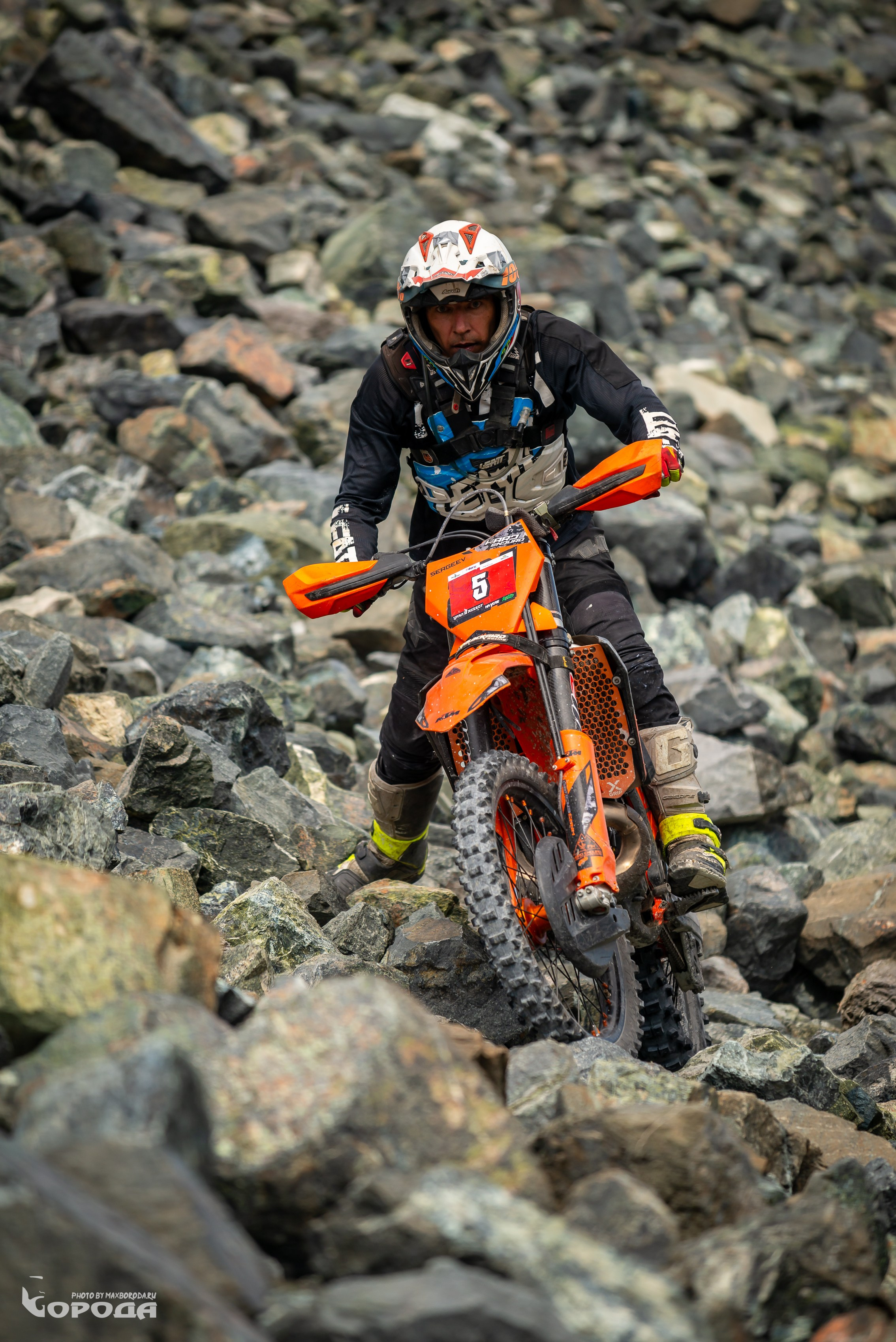 Спортсмен на оранжевом байке преодолевает каменистую преграду, номер 5.