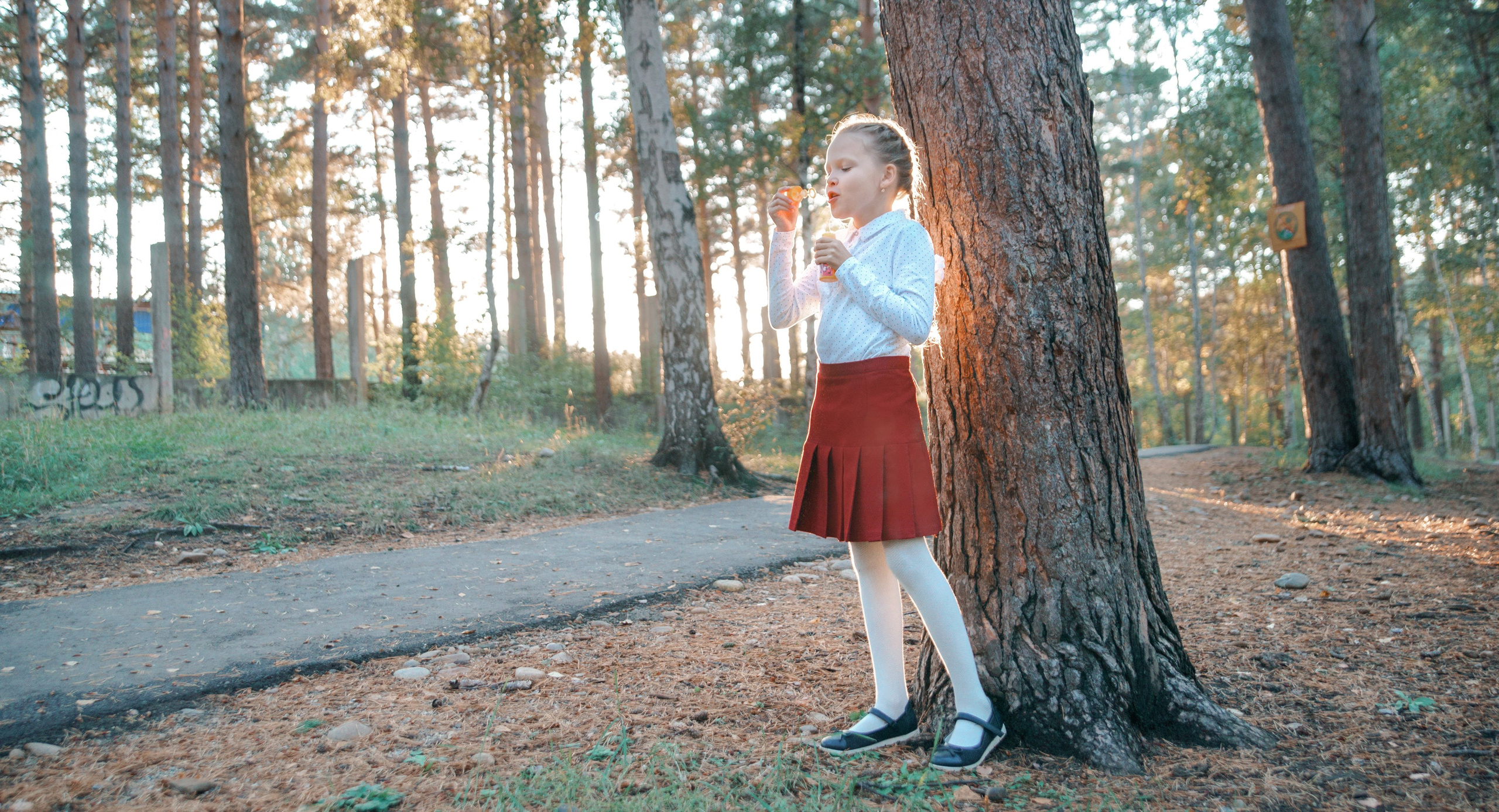 Детская фотосессия осенью - школьница стоя у дерева дует мыльные пузыри