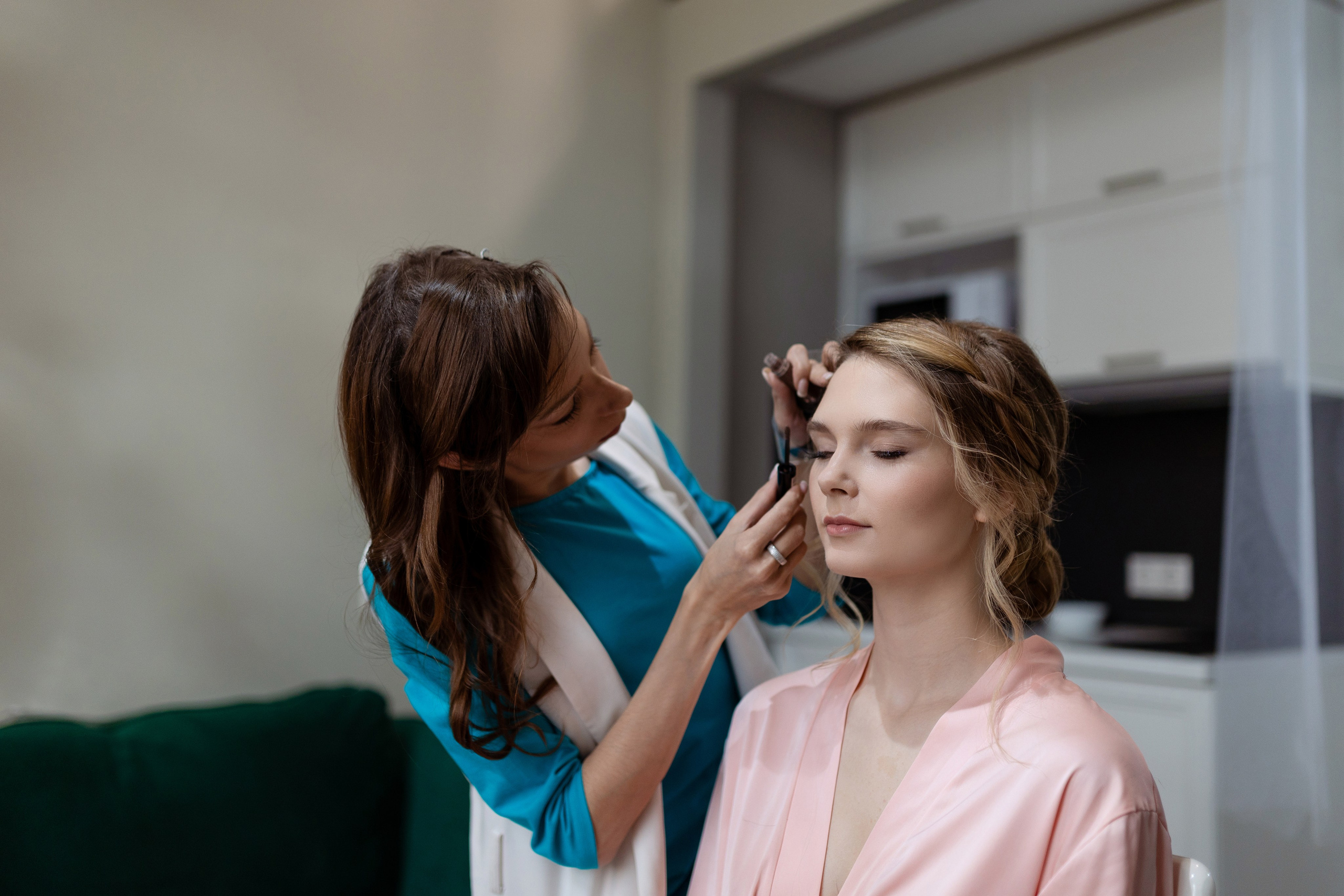 Визажист поправляет прическу невесте и заканчивает макияж.