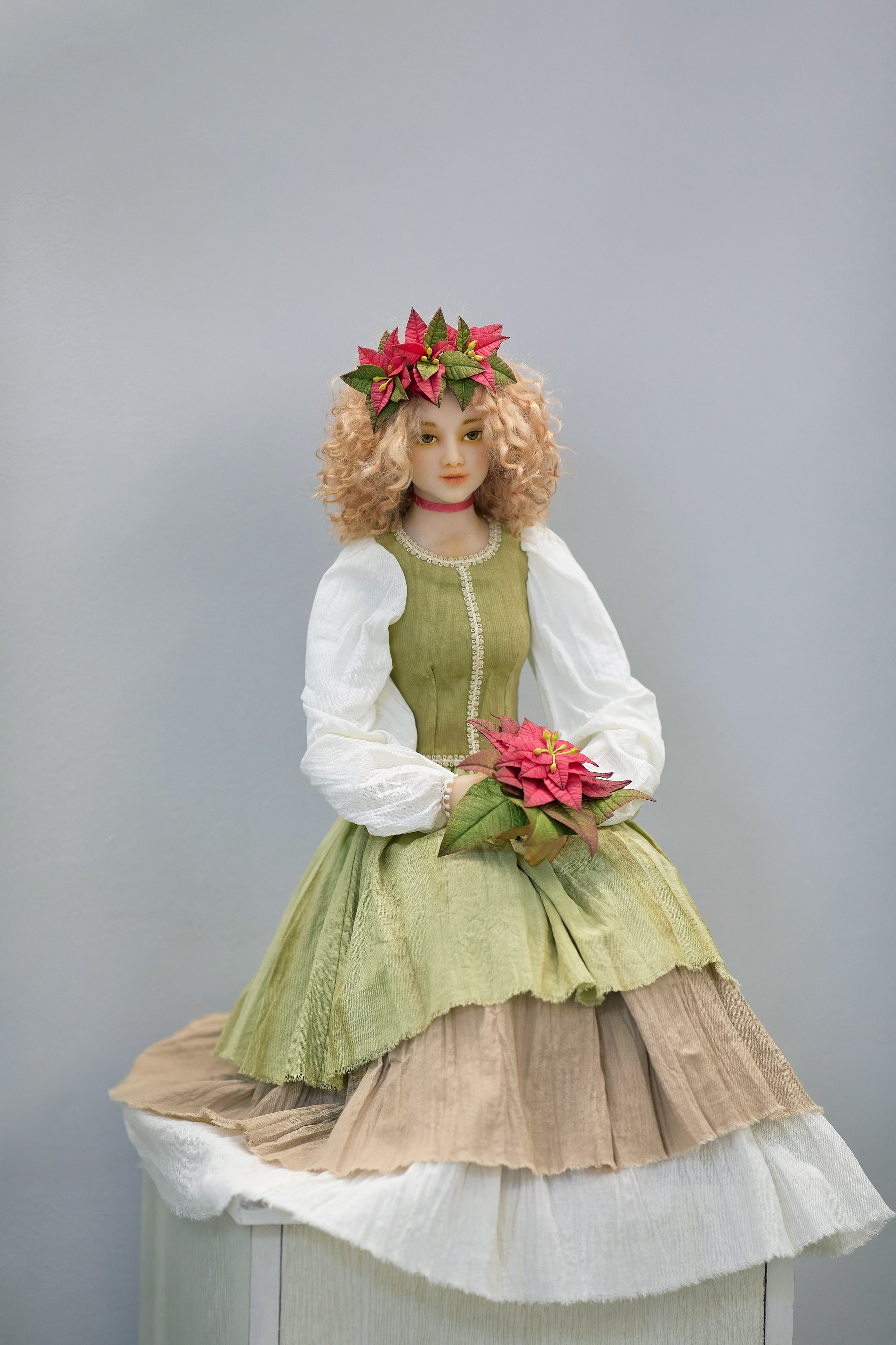 Кукольная женщина в зеленом платье с цветами в волосах и в руках, сидящая на подставке