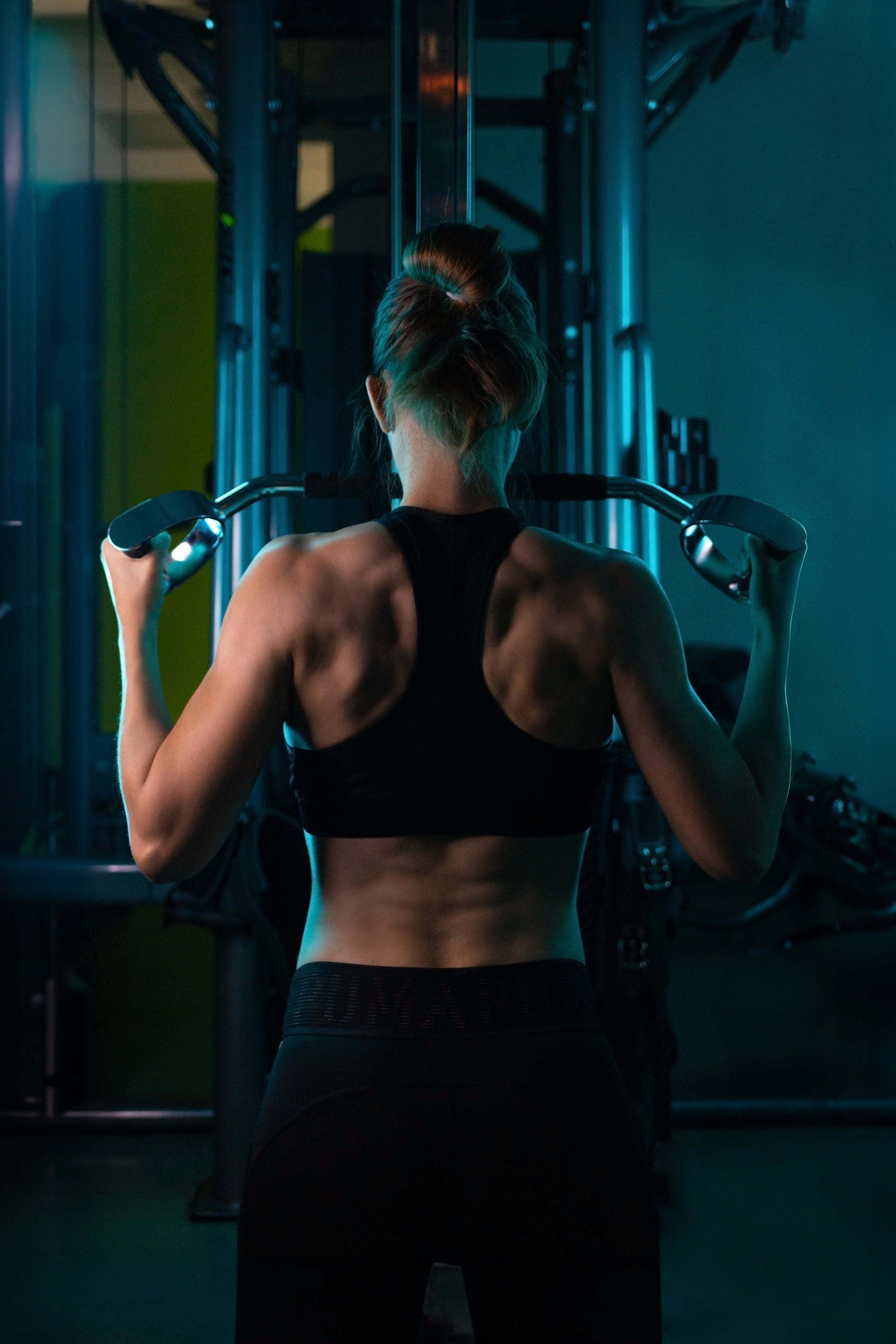Накаченная женская спина. Фото красивой спортивной женской спины в спорт фитнес зале в бирюзовых голубых цветах.