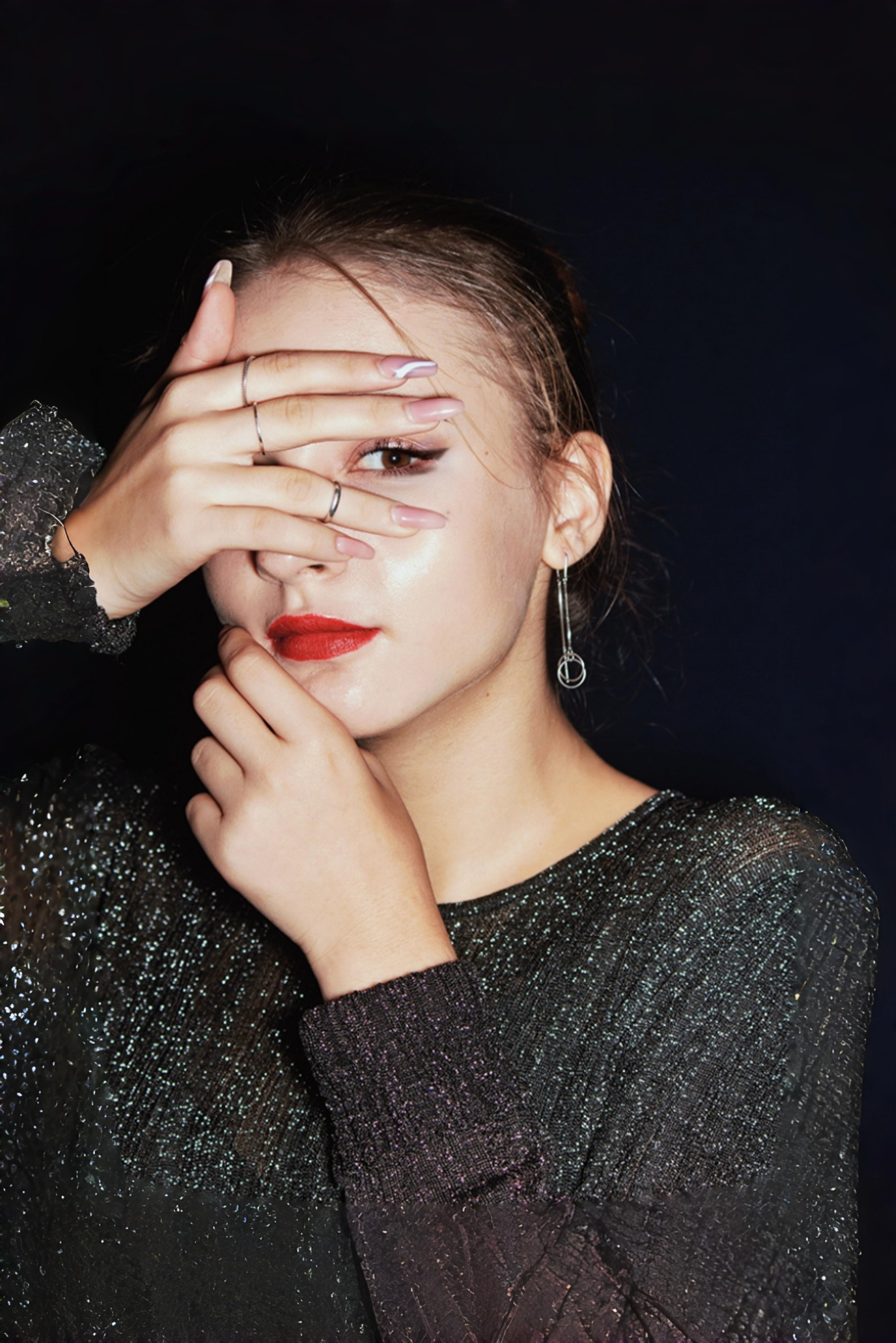 Цветная креативная фотография девушки 14 лет - глаза частично закрыты ладонью, другая рука прикрывает подбородок. Девушка одета в черный люрекс, на губах яркая красная помада, глаза оформлены черным цветом - это гранж-образ.