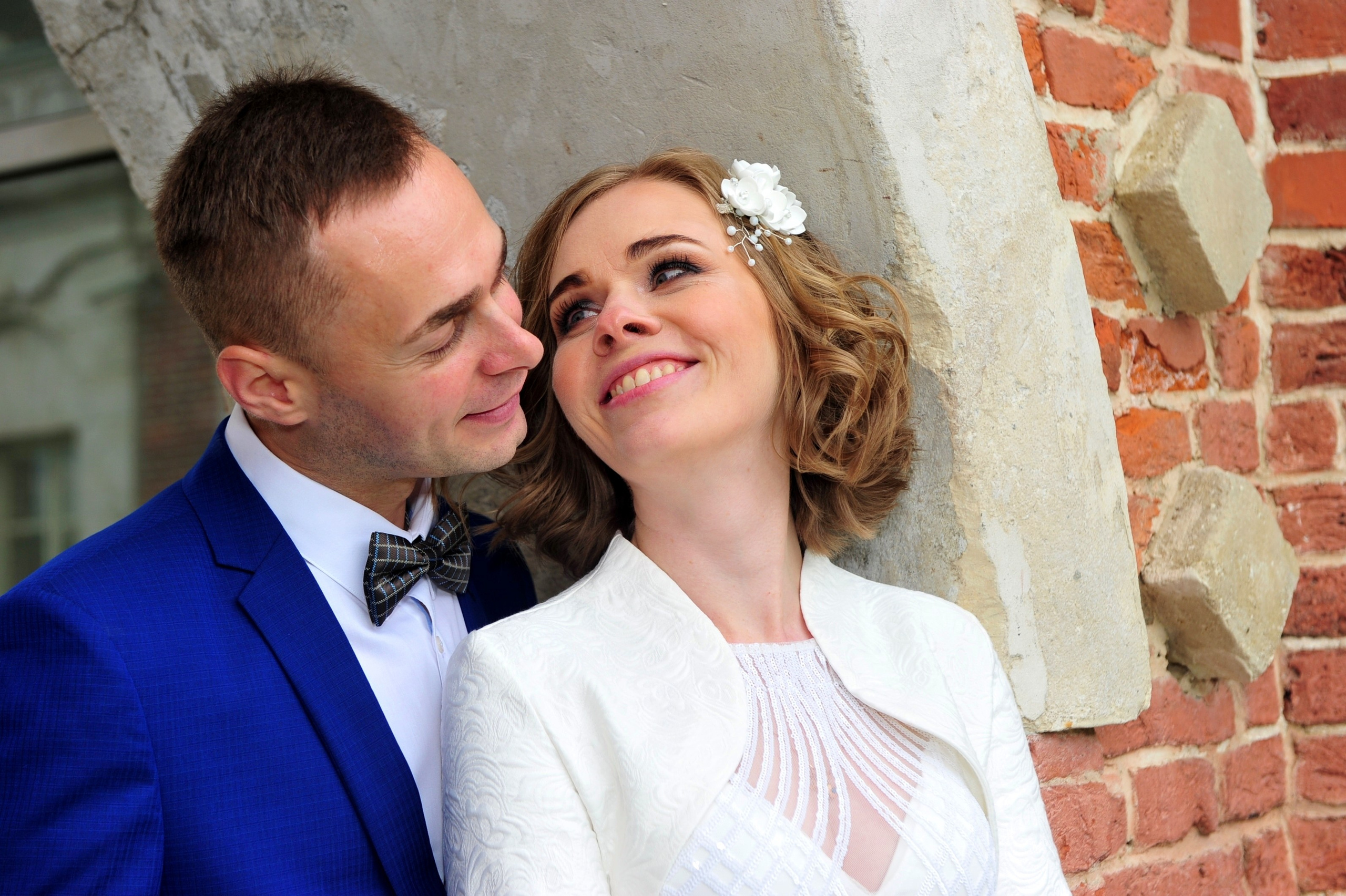 Свадьба в Царицыно хмурым прохладным летним днём, новобрачные у красной кирпичной стены, жених смотрит на губы невесты