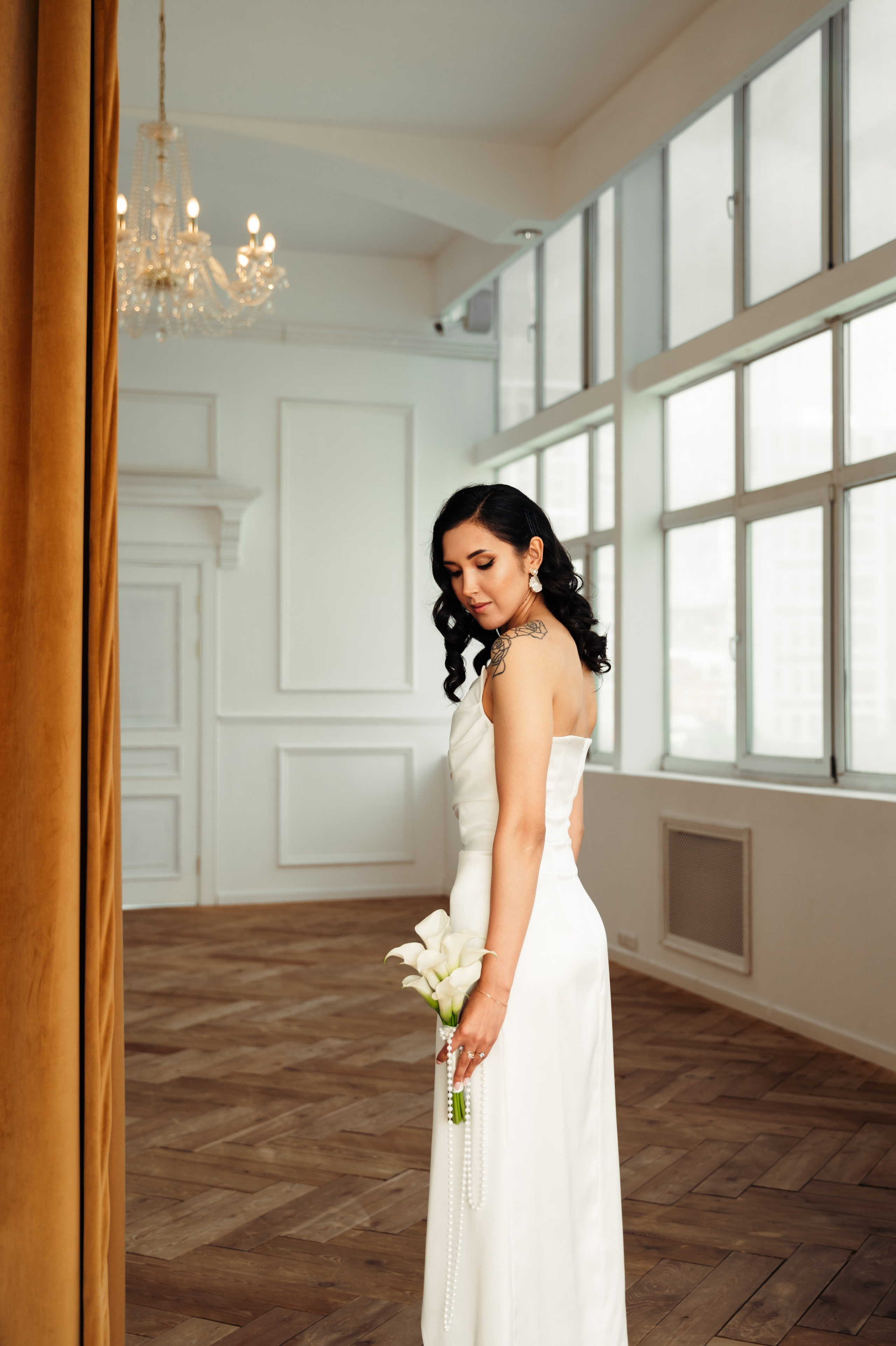 невеста в приталенном белом платье с букетом коал в роскошной фотостудии с хрустальной люстрой