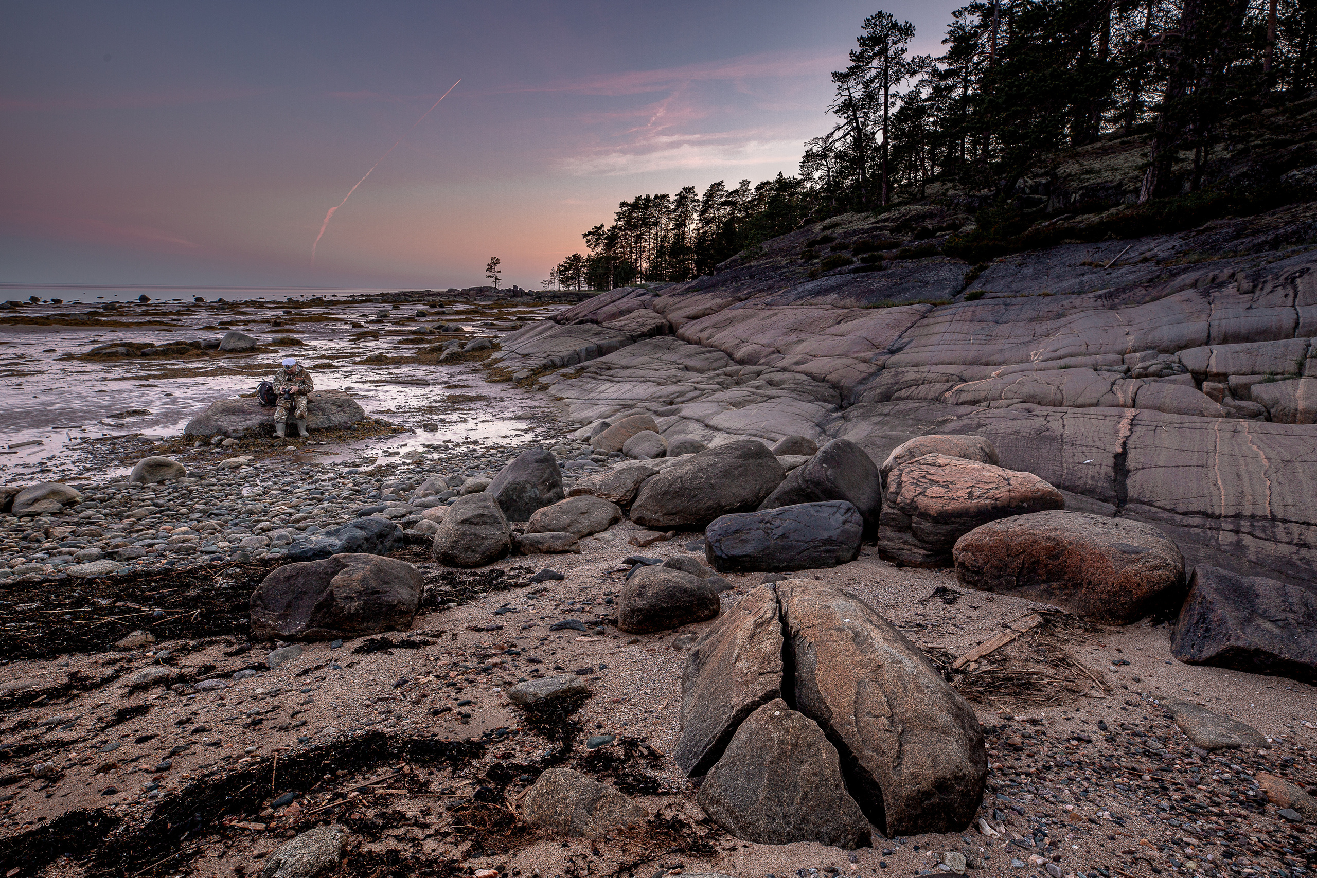 мужчина читает книгу, сидя на камне на острове белой ночью. 