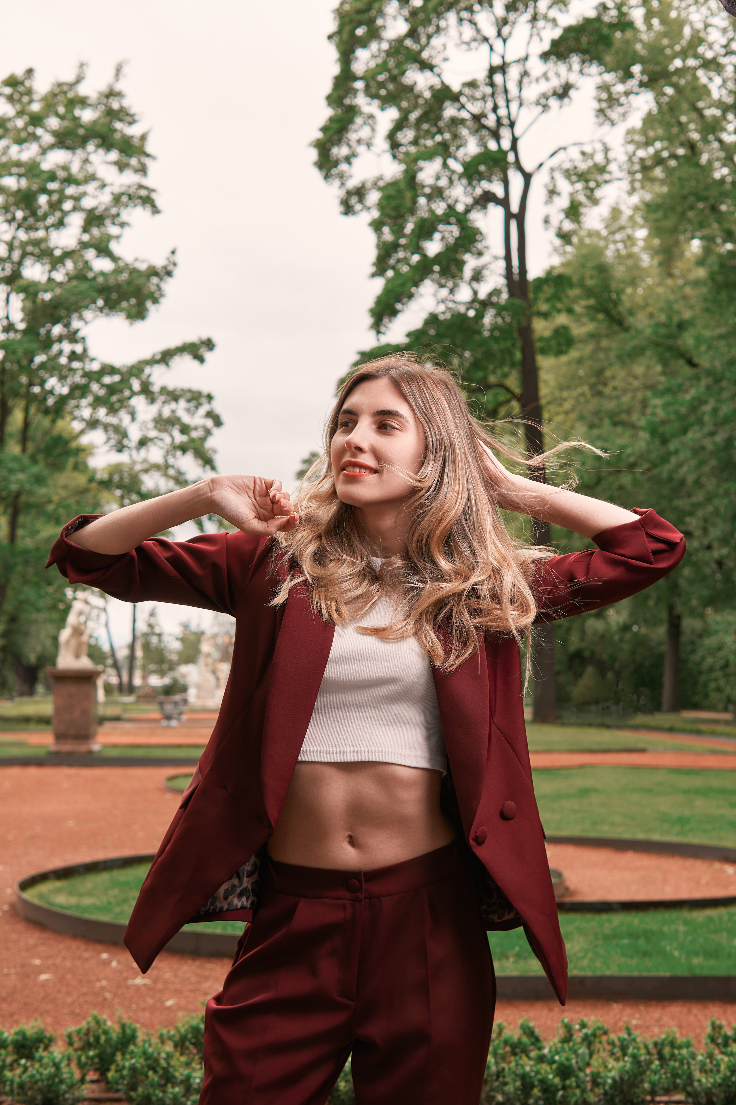 прогулочная фотосессия девушки в бордовом костюме в летнем саду со вспышкой летом в зелени в Санкт-Петербурге в стиле кино, стробизм днем в пасмурную погоду