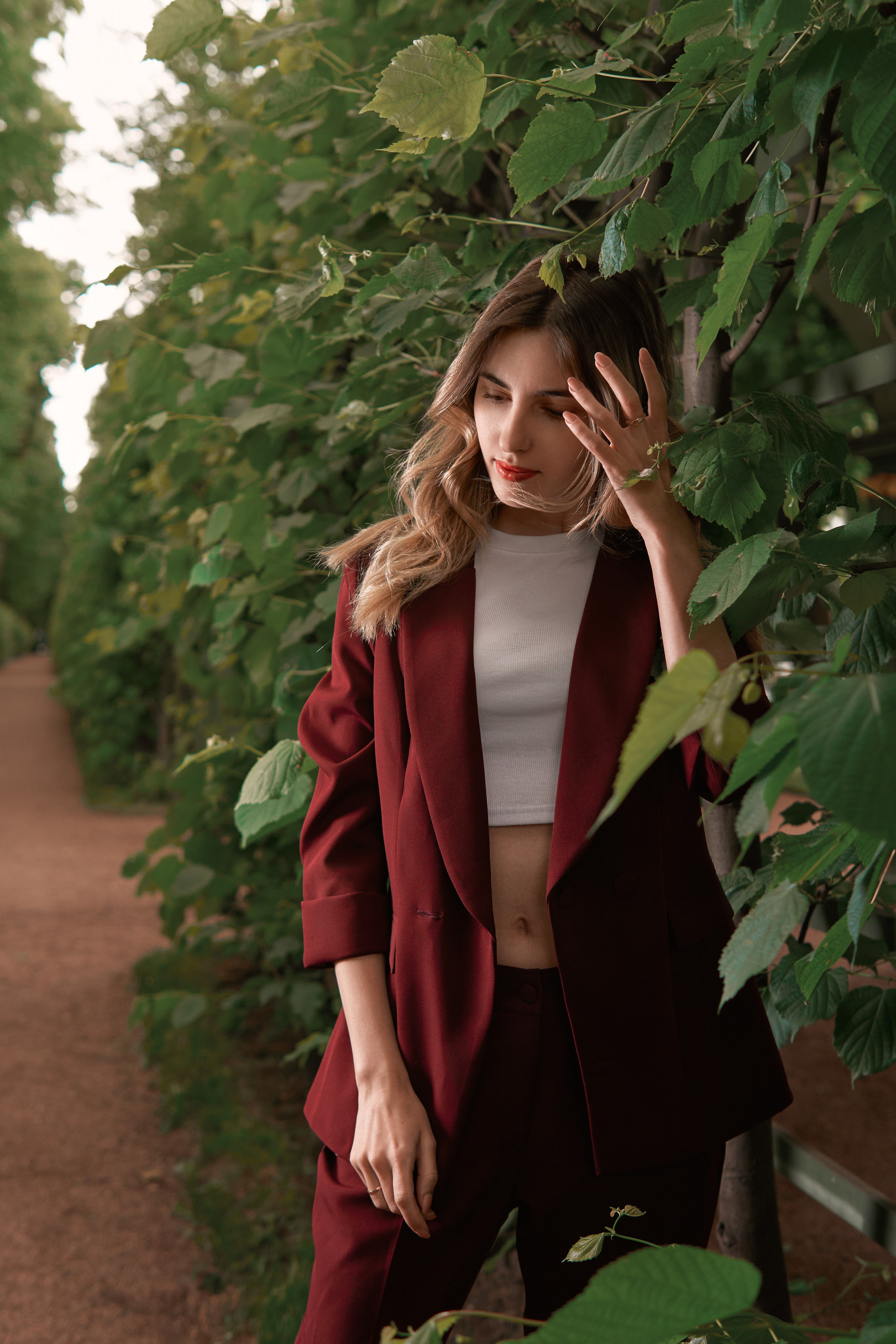 прогулочная фотосессия девушки в бордовом костюме в летнем саду со вспышкой летом в зелени в Санкт-Петербурге в стиле кино, стробизм днем в пасмурную погоду