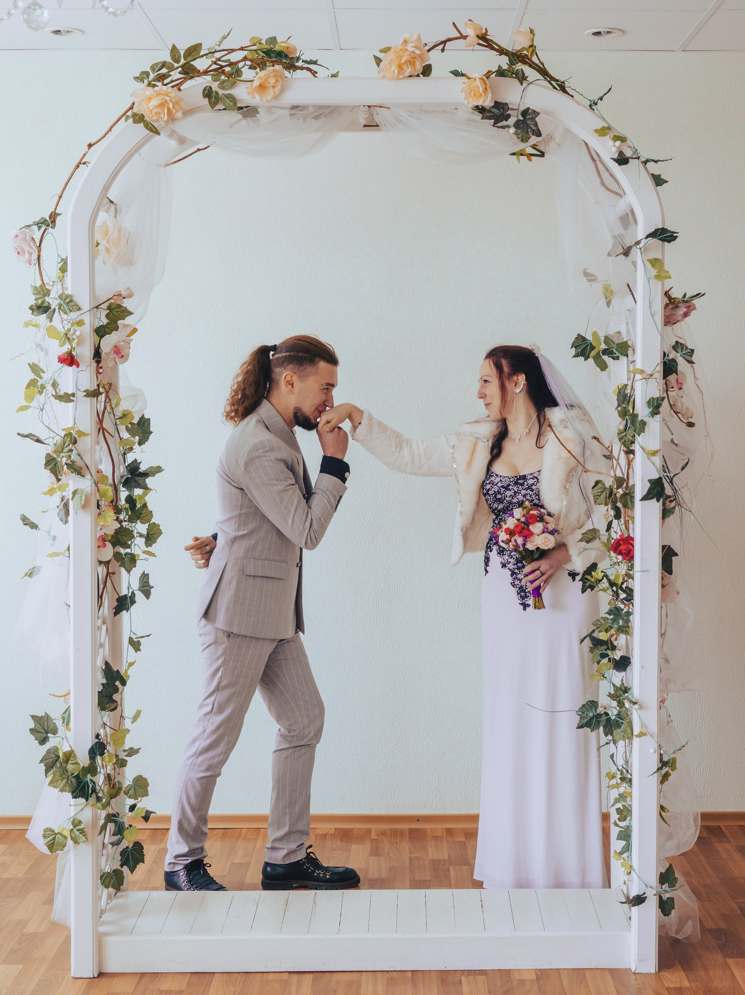 жених целует руку невесты за аркой молодых