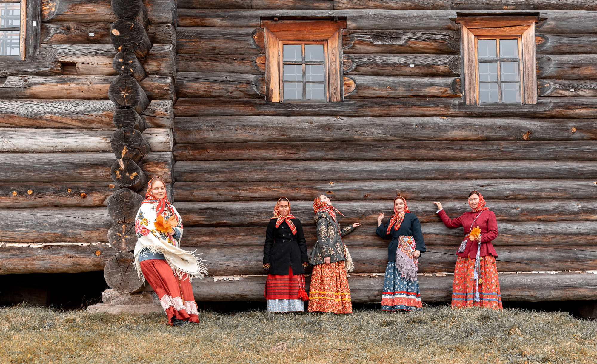 Девушки с старинных русских нарядах под окнами высокого северного деревянного дома. 