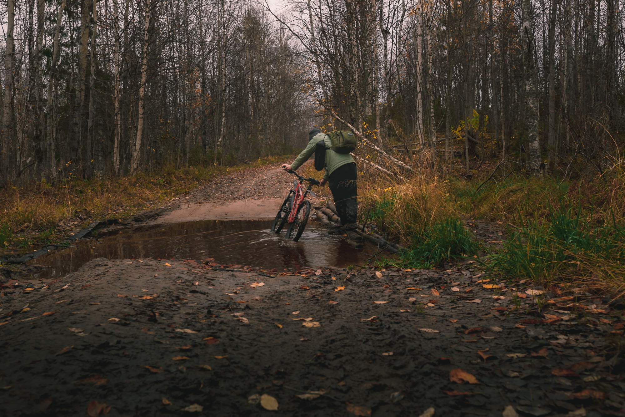 Мужчина на велосипеде переезжает большую лужу на лесной дороге. 