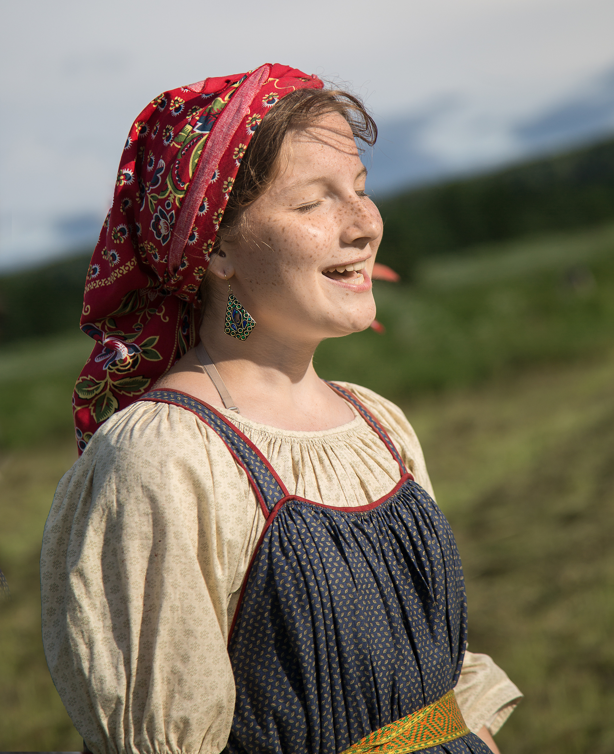 Девушка в русском синем сарафане и красном платке поет песню.