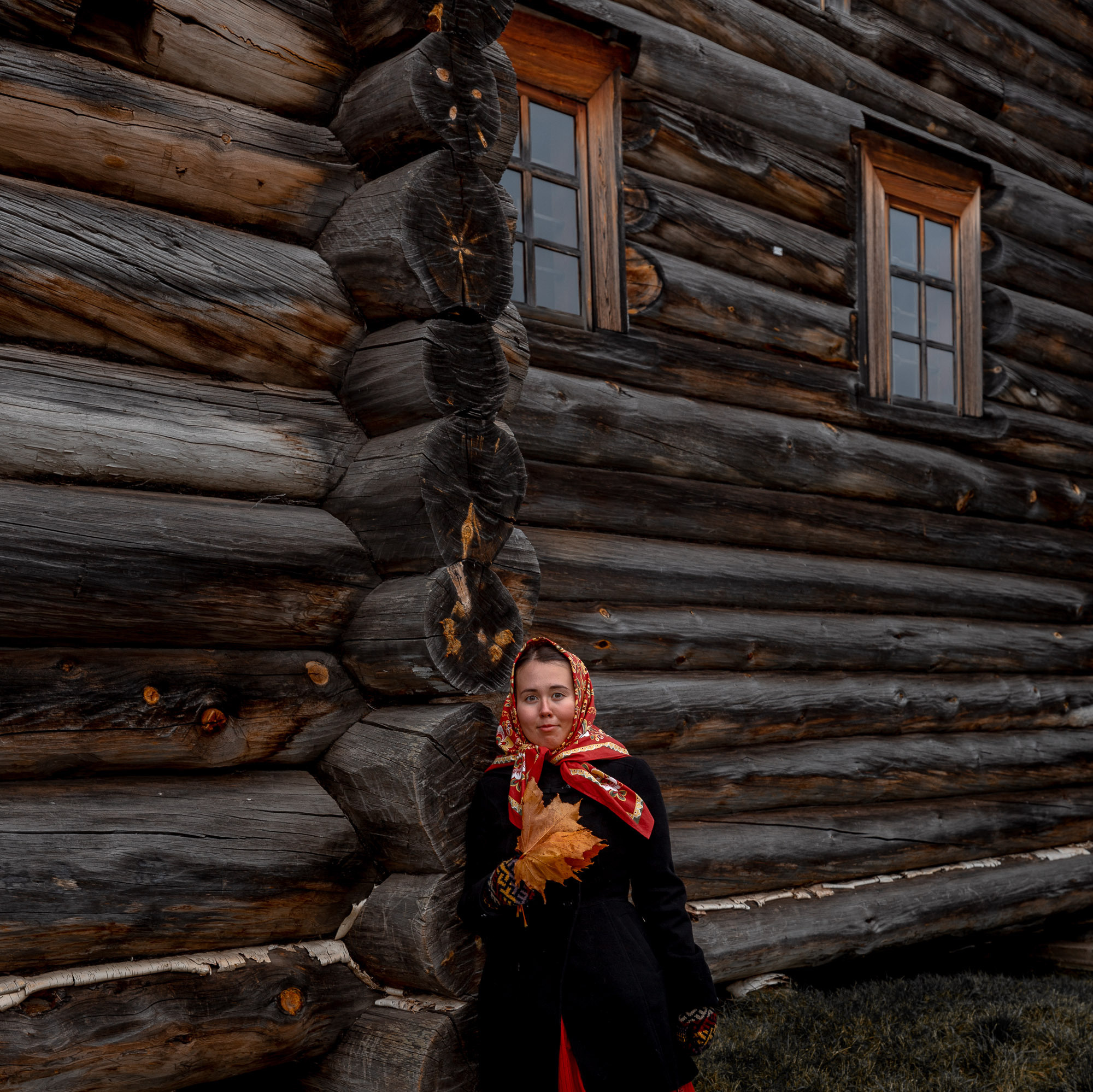 Деревенская девушка в красном платке в народном русском костюме 19 века у деревянного северного дома. 