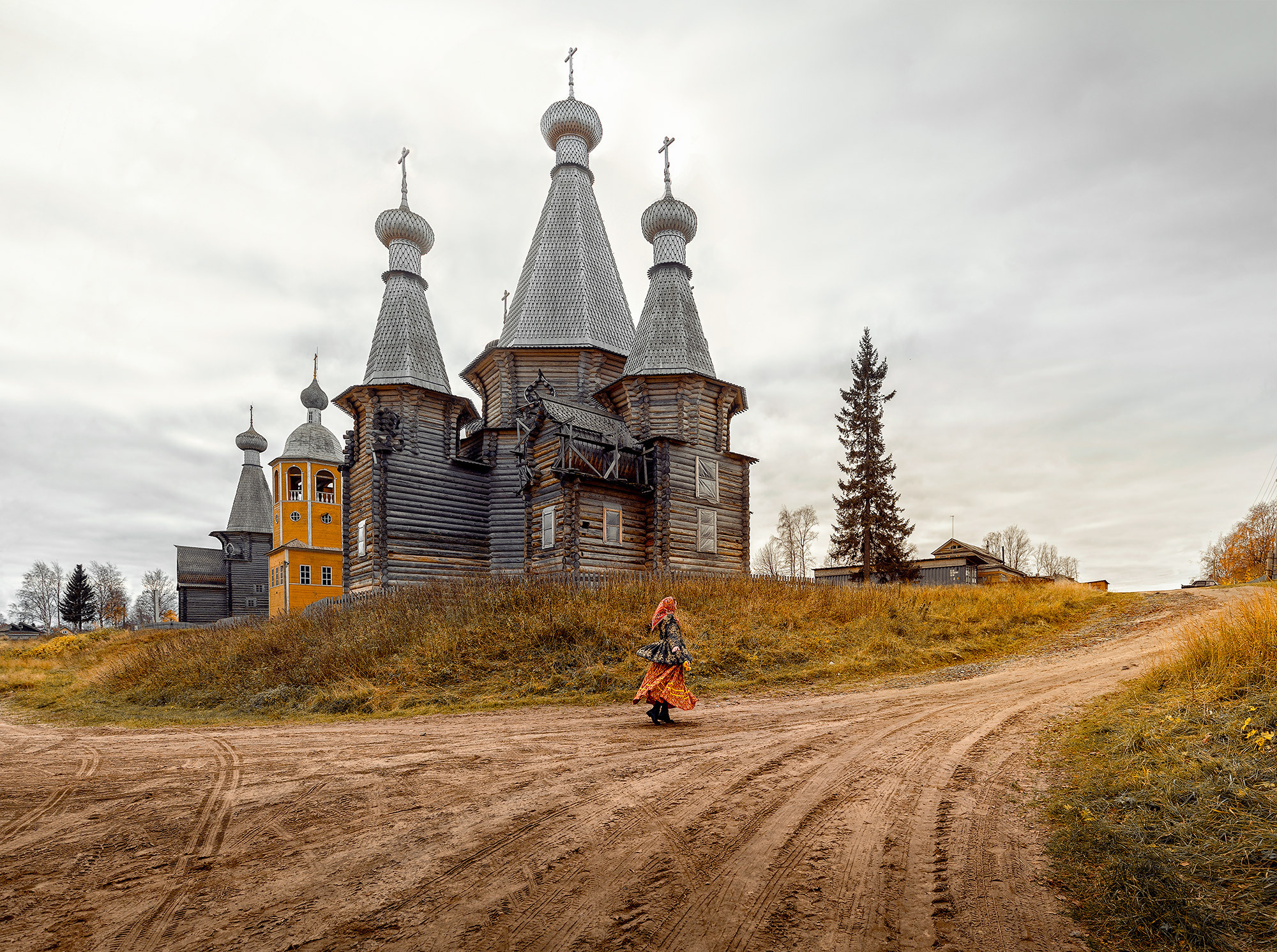 Девушка в старинном наряде, бежит по деревенской дороге мимо храма села Ненокса. 