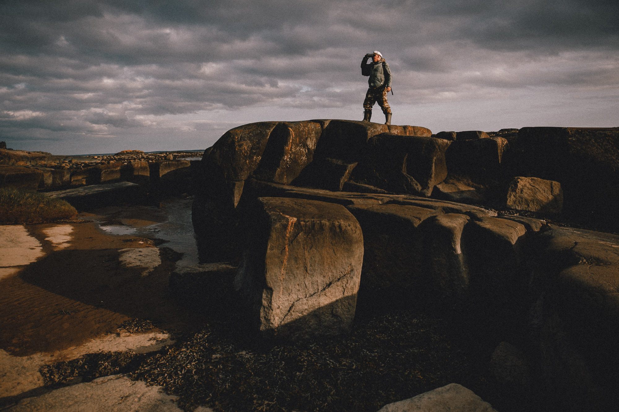 Мужчина смотрит в бинокль на скалах Кий острова. 
