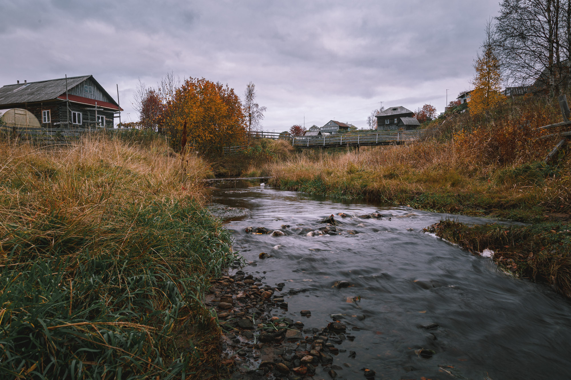 Каменистый ручей бежит по северной деревне осенью. 