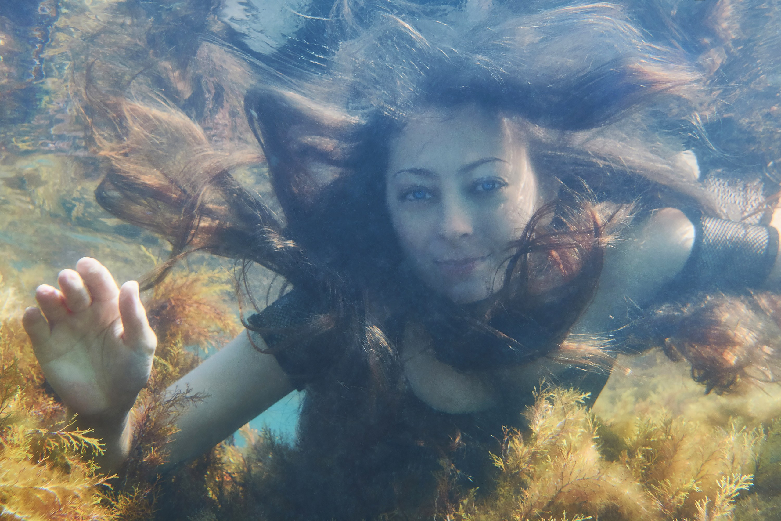 Девушка плывет под водой среди водорослей