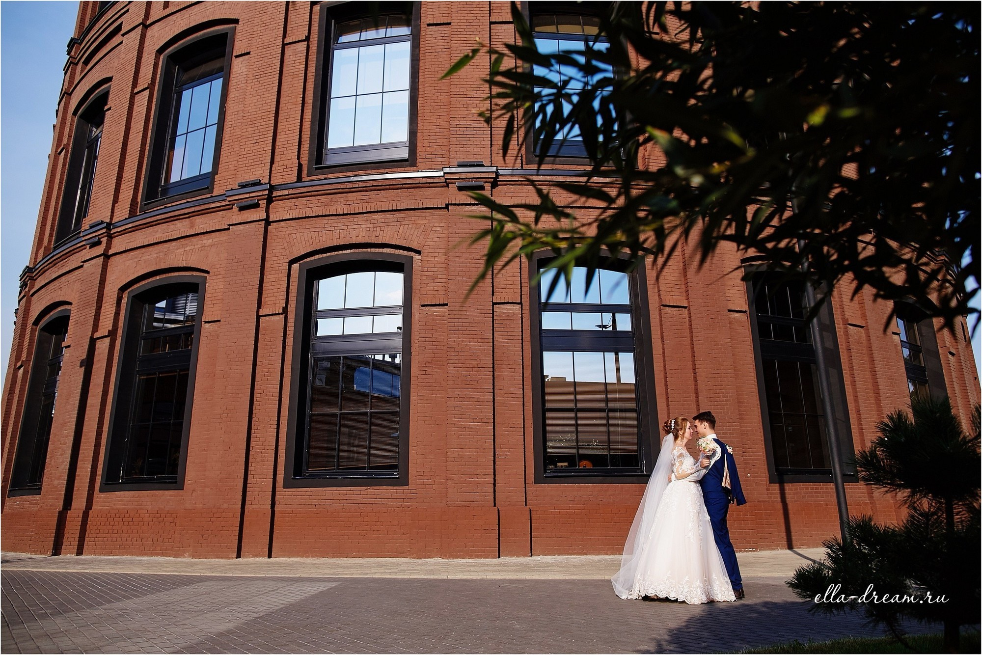 Молодожены на фоне дерева и кирпичного здания