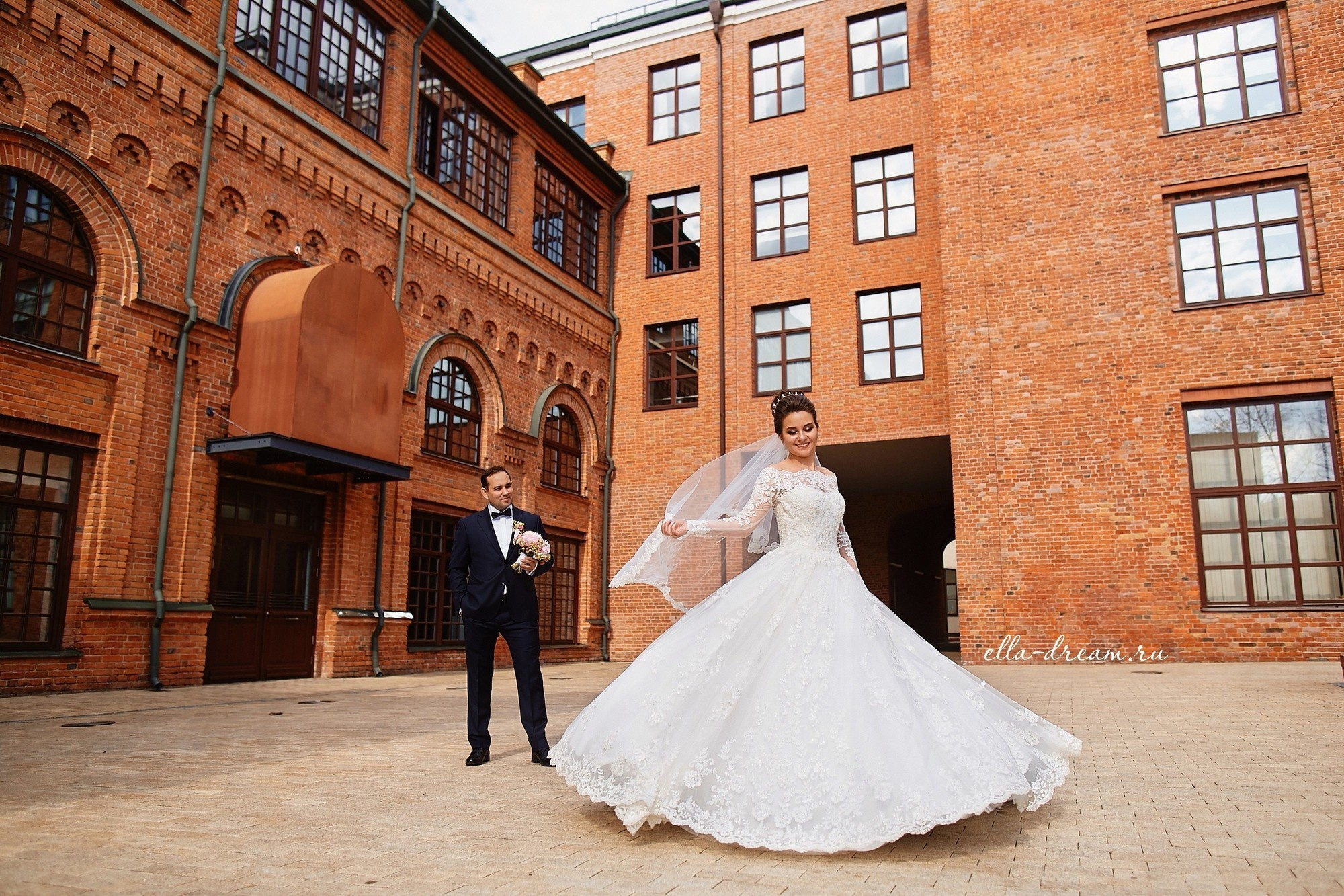 Невеста кружится перед женихом на фоне кирпичной стены