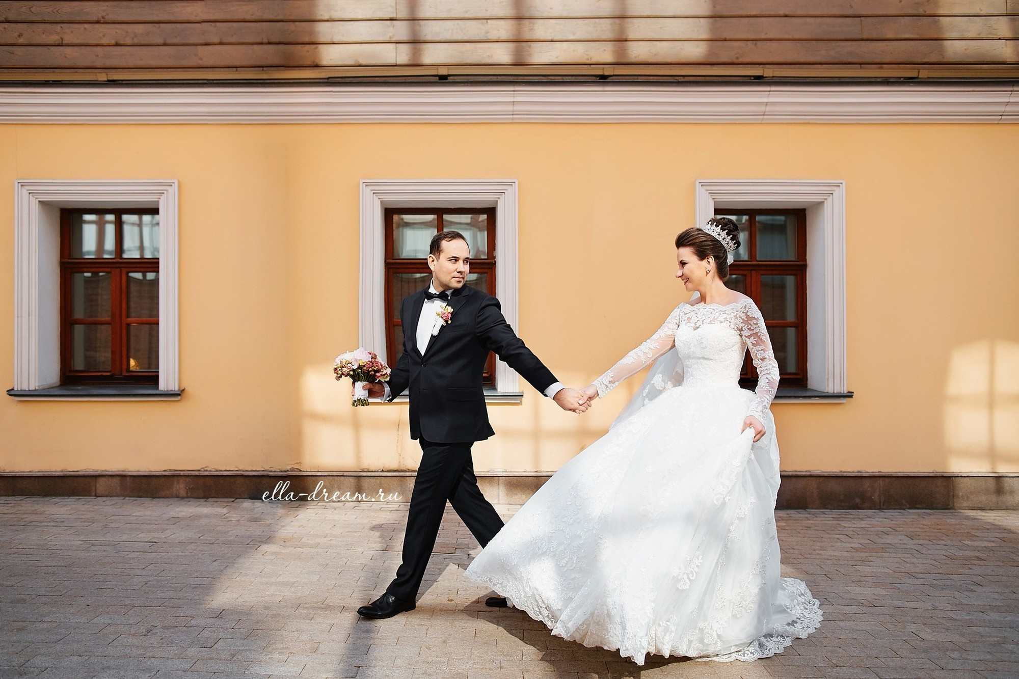 Жених с невестой радостные гуляю по улице на фоне дома 