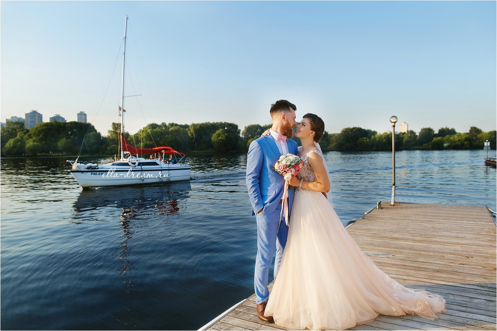 Жених в голубом костюме с красивой невестой на фоне реки и корабля и лодки