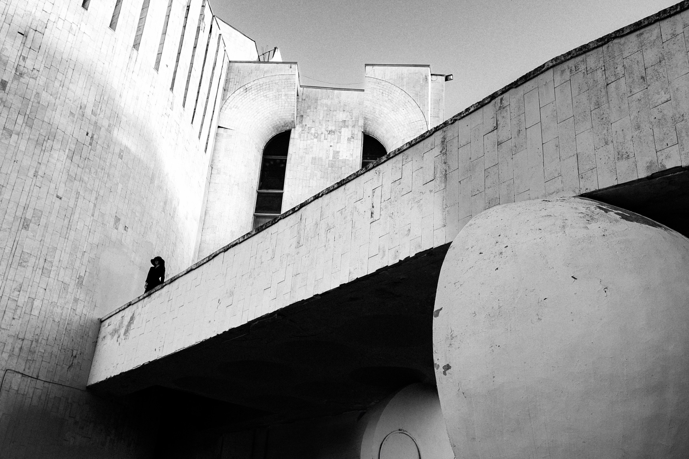Фигура женщины в чёрной одежде на фоне монументального здания, чёрно-белая арт-фотография с архитектурным акцентом