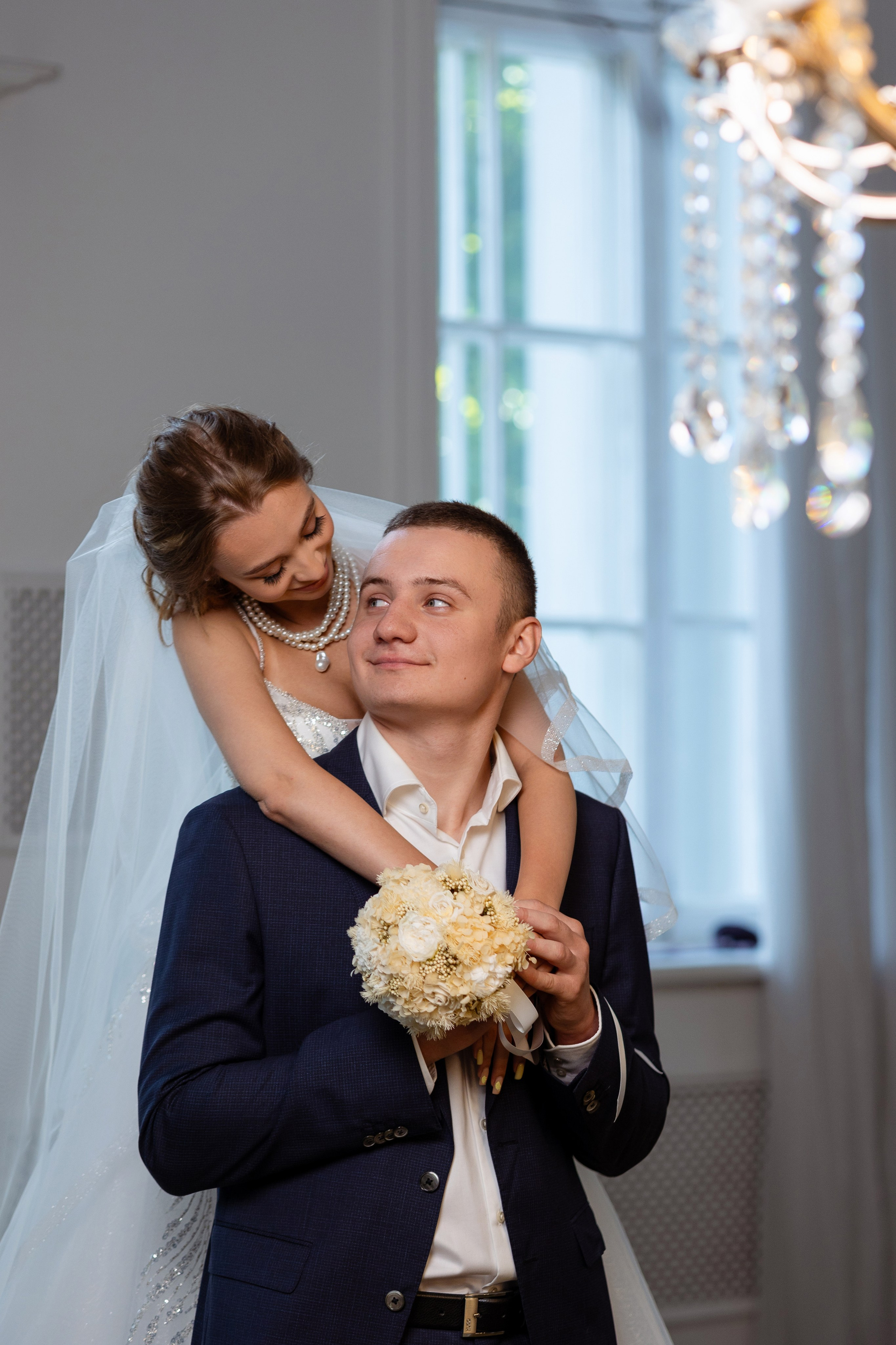 Невеста стоя за женихом обняла его обеими руками.