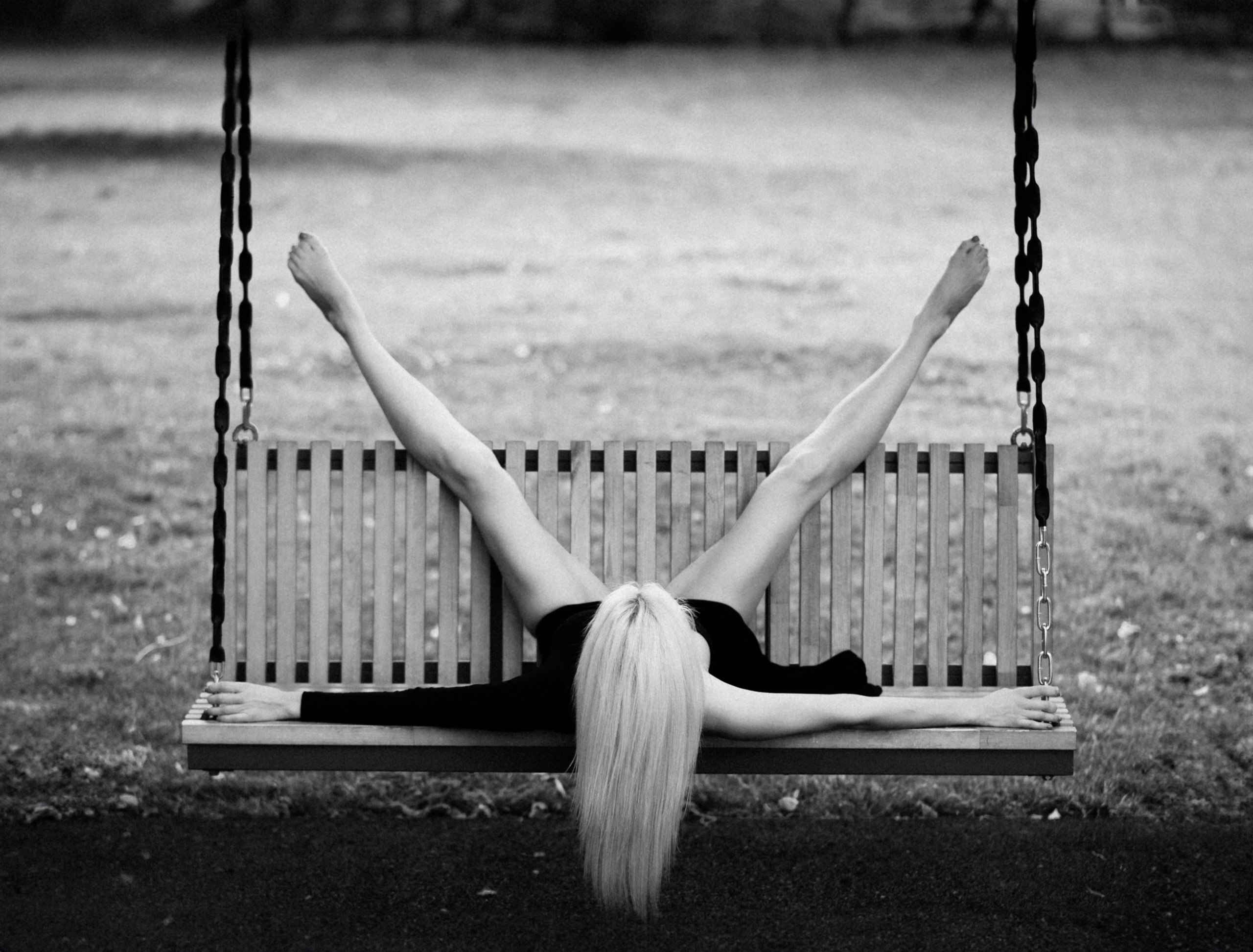 Девушка лежит на качелях ногами вверх.