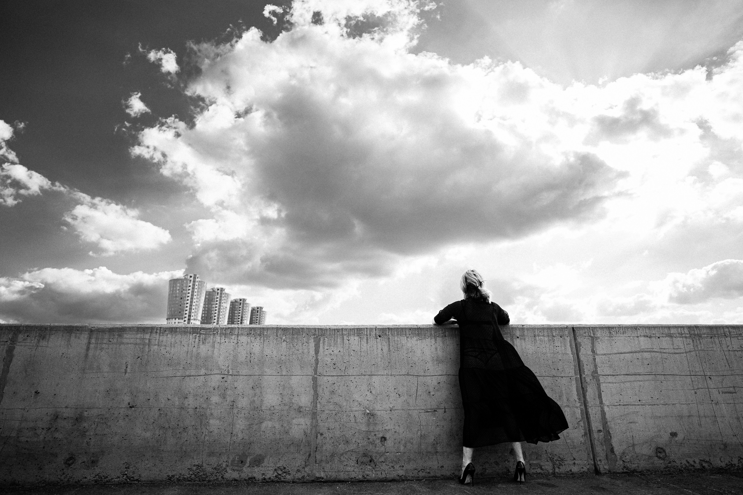 Девушка стоит на фоне города и облаков.