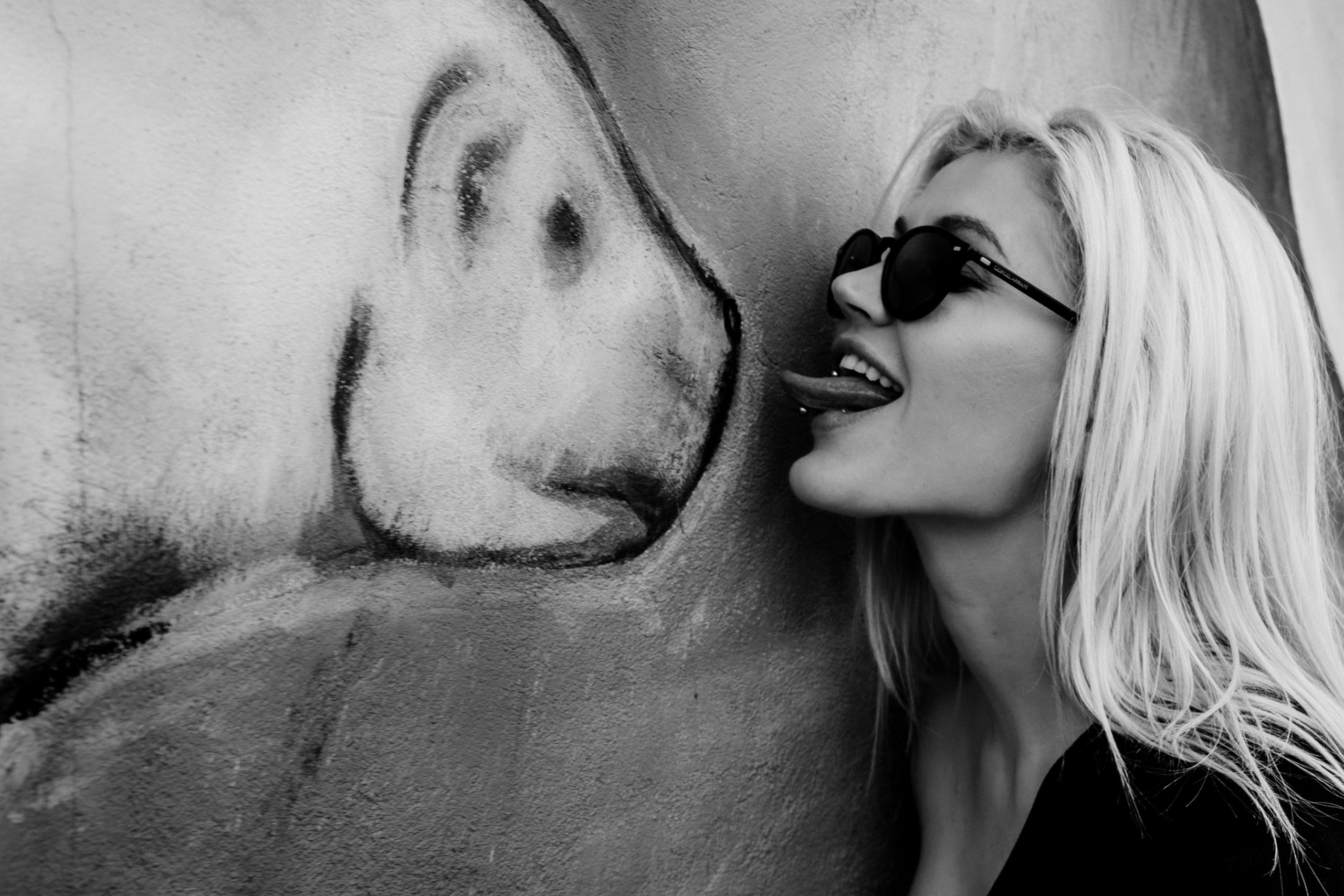 Девушка в тёмных очках облизывает граффити.