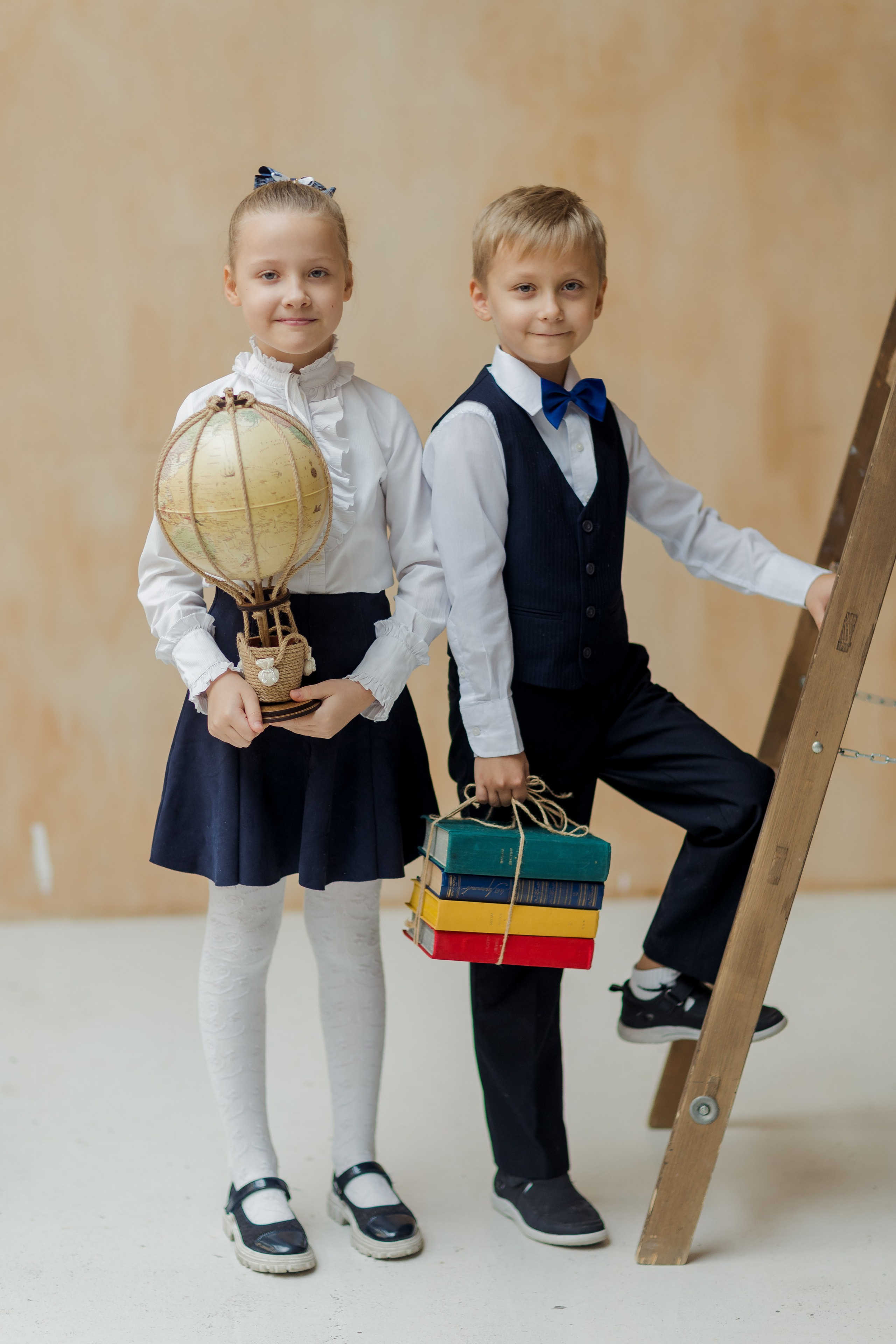 Мальчик и девочка стоят около лестницы с книгой и глобусом