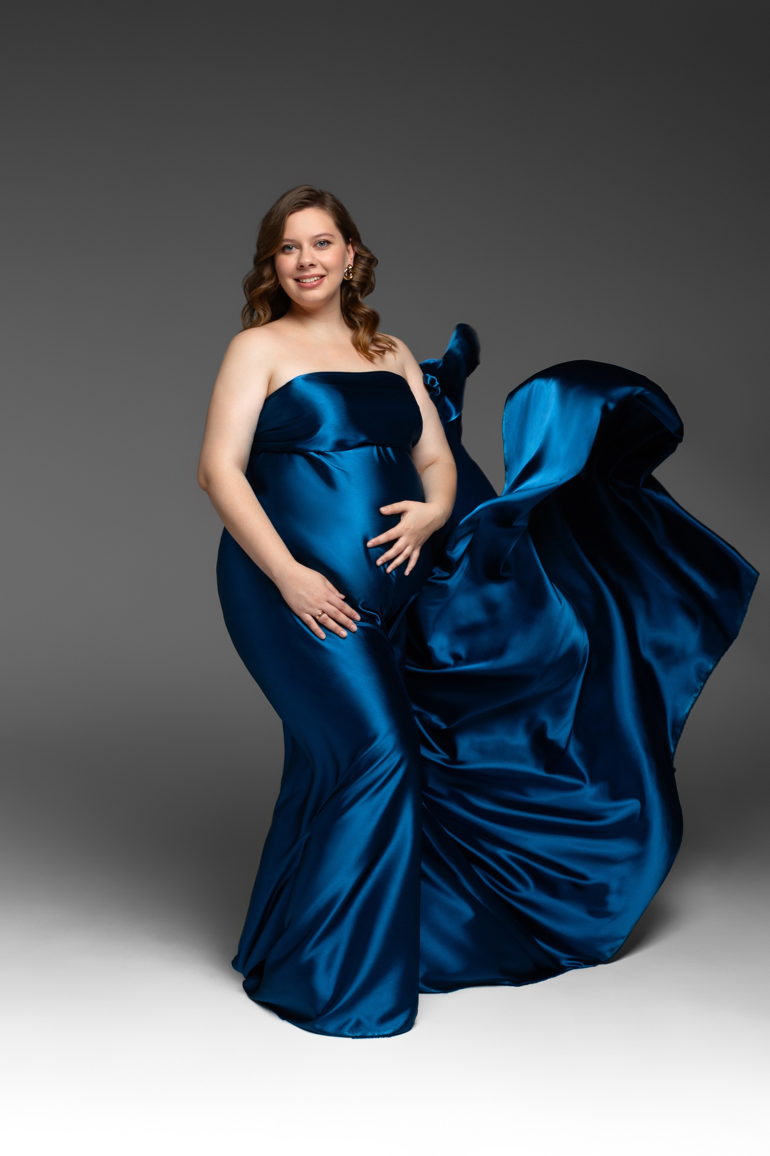 Беременная девушка в шелковой синей ткани, которая развивается за ее спиной 