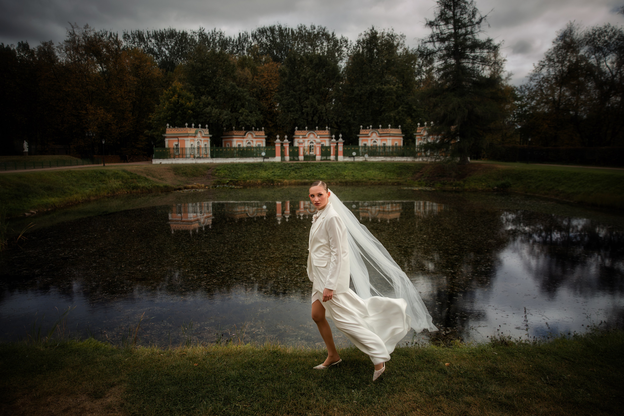 Невеста в белом костюме идёт вдоль пруда с отражением дворца, лёгкая фата развевается на ветру, усадьба Кусково.