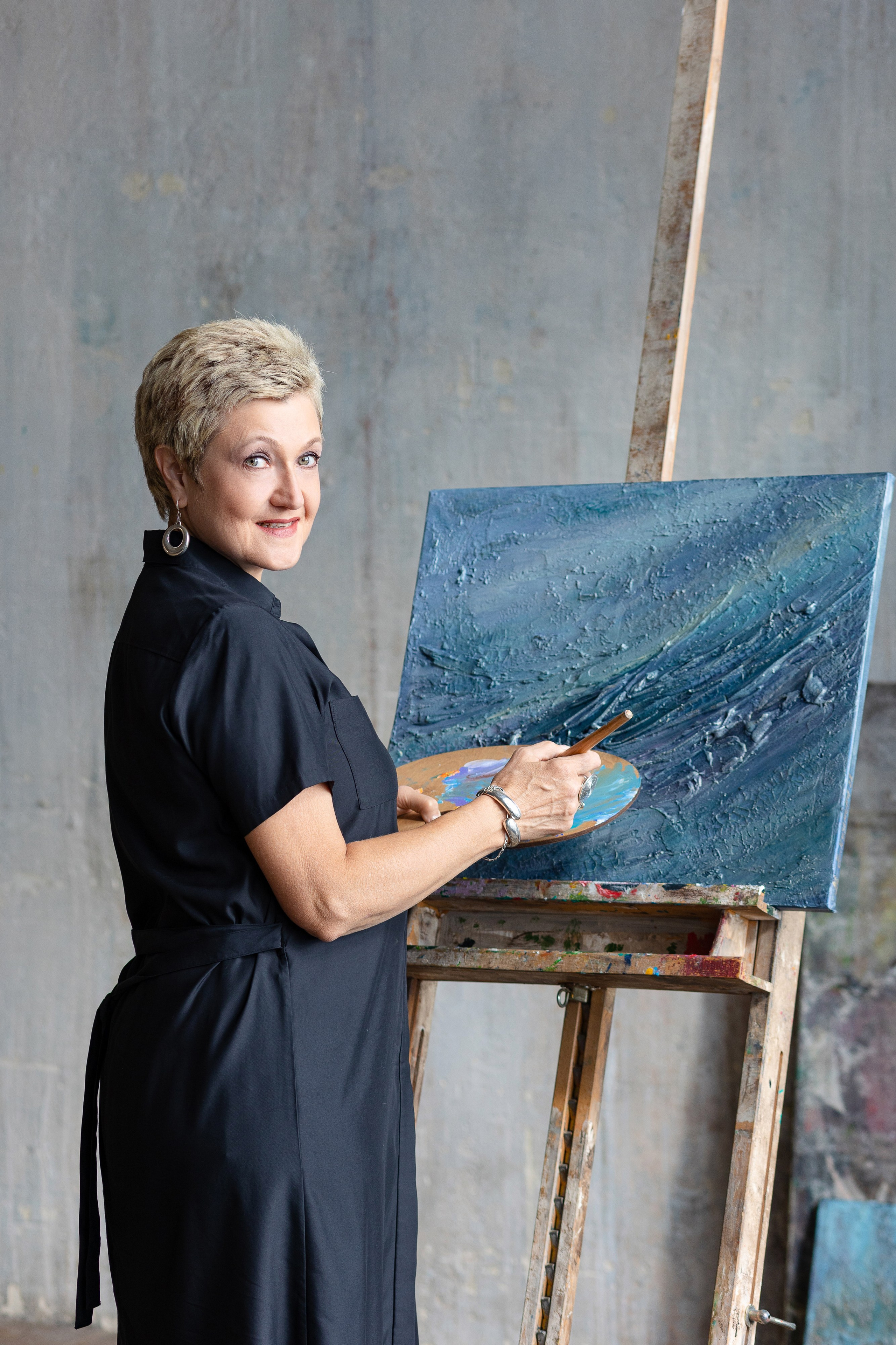 Женщина с палитрой в руках стоит у пюпитра, на котором находится картина.