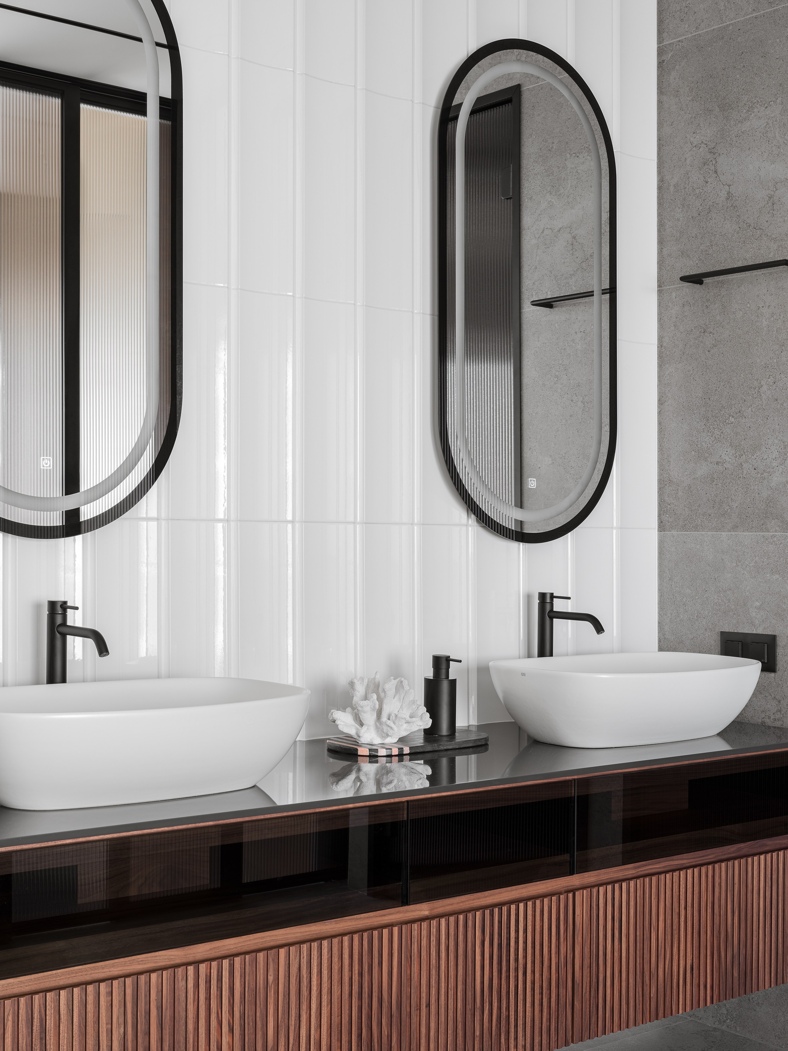 Стильная ванная комната с двойной раковиной, подвесной тумбой из дерева с вертикальными фасадами, овальными зеркалами в черных рамах и минималистичной сантехникой. Авторство Рената Байчукова и Алеси Кириенко, стилист Екатерина Ракитина, фотограф Сергей Денисенко.