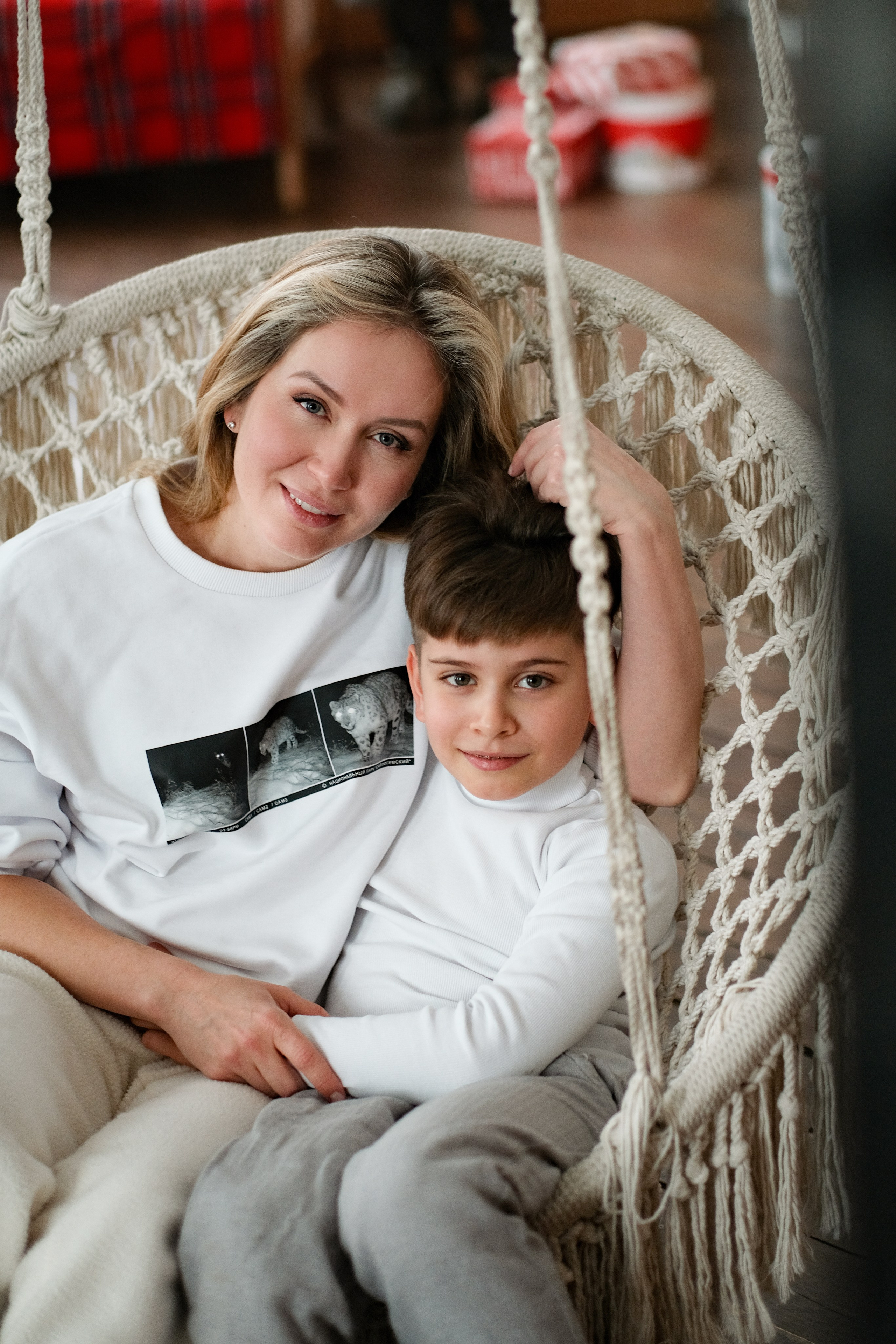 Мама с сыном в светлой одежде сидят на качелях.