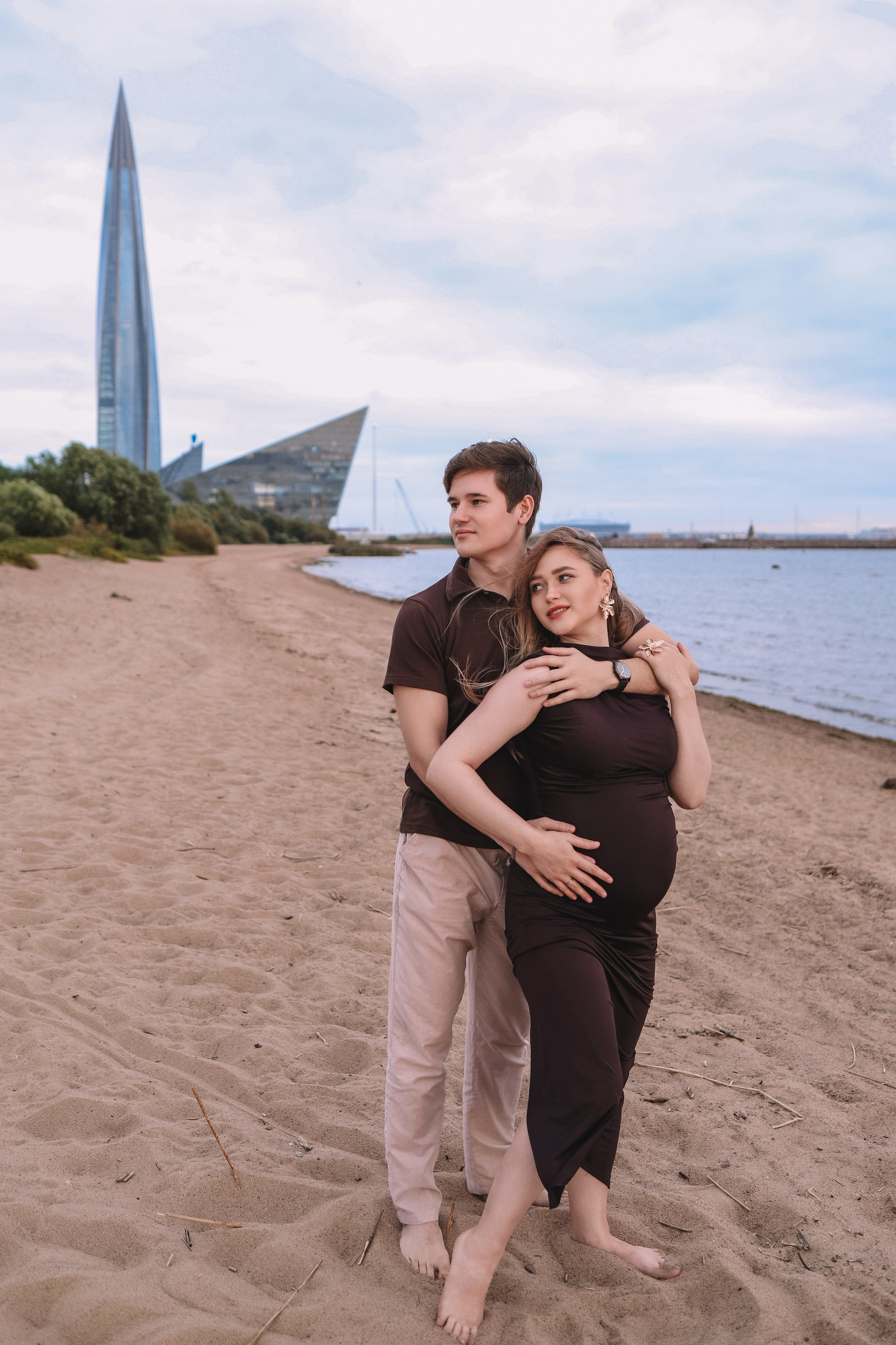 Пара идёт по песку у воды, фотосессия беременности