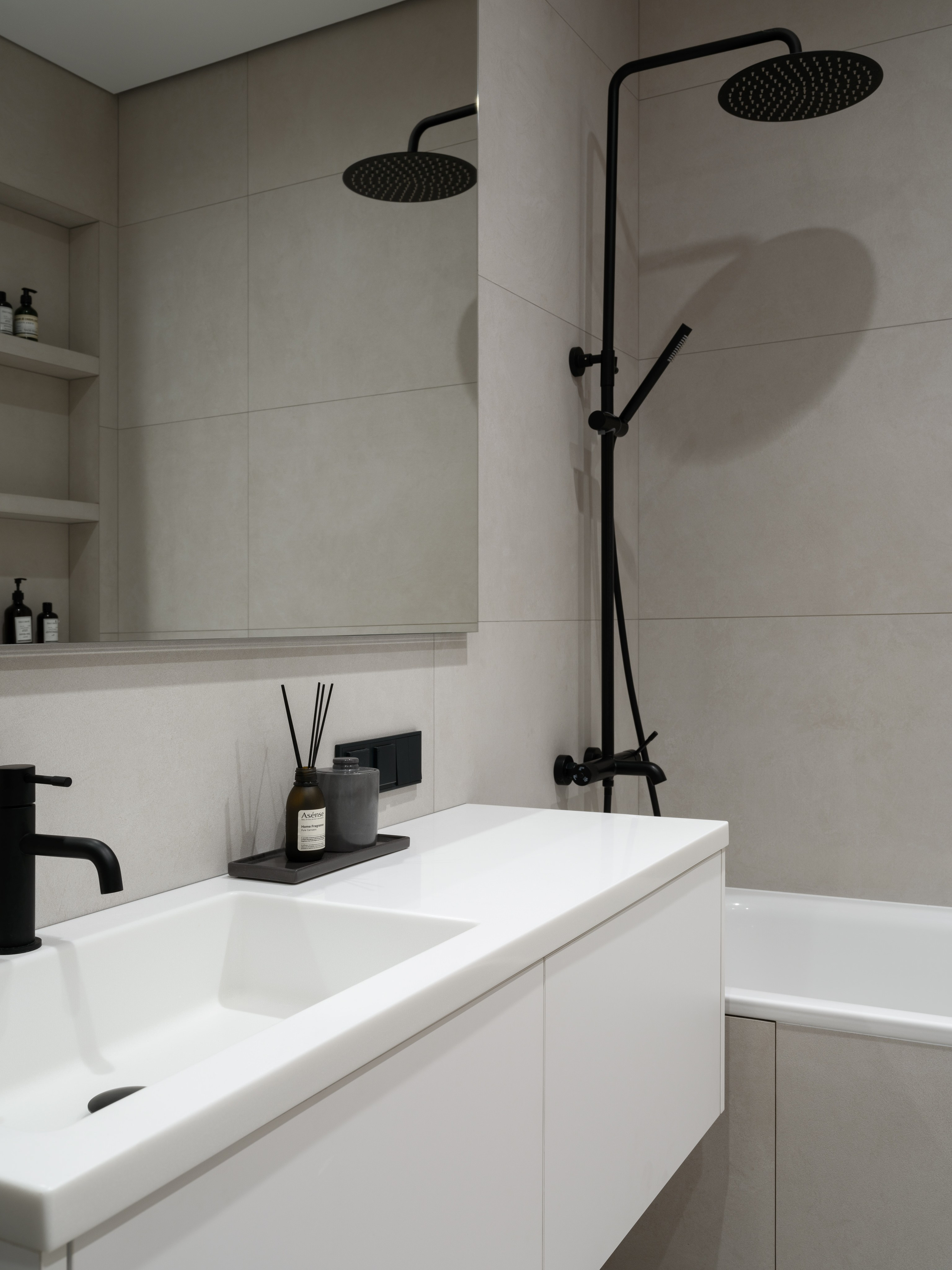 Современная ванная комната в минималистичном стиле с белым умывальником, подвесной тумбой и черным душевым комплектом. Автор проекта — дизайнеры Евгения Княжева и Владлена Привалова, фотограф Сергей Денисенко